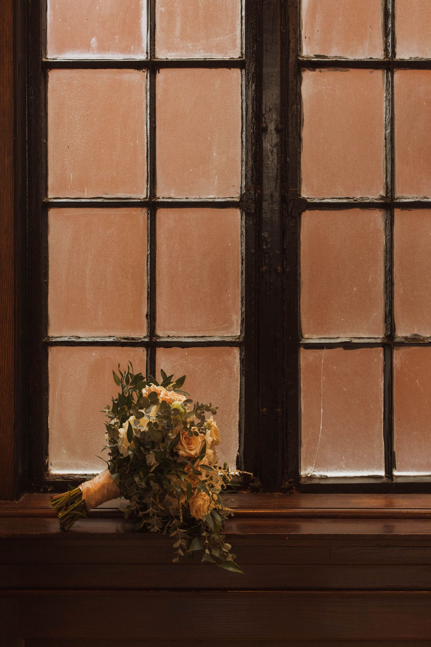Romantic bridal bouquet sits against warm-toned windowpanes in vintage setting.