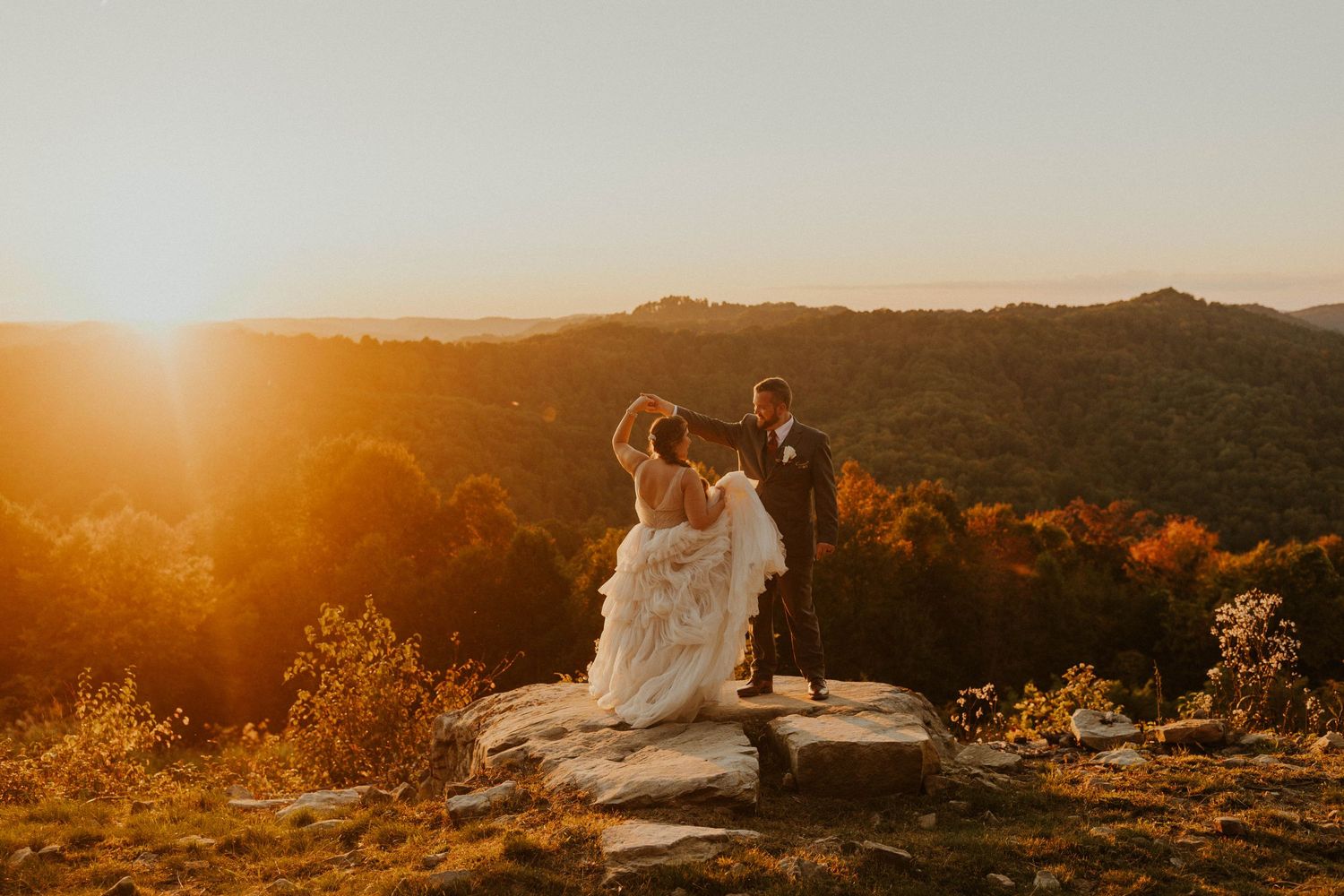 A couple sharing a romantic moment on a clifftop overlook during sunset.