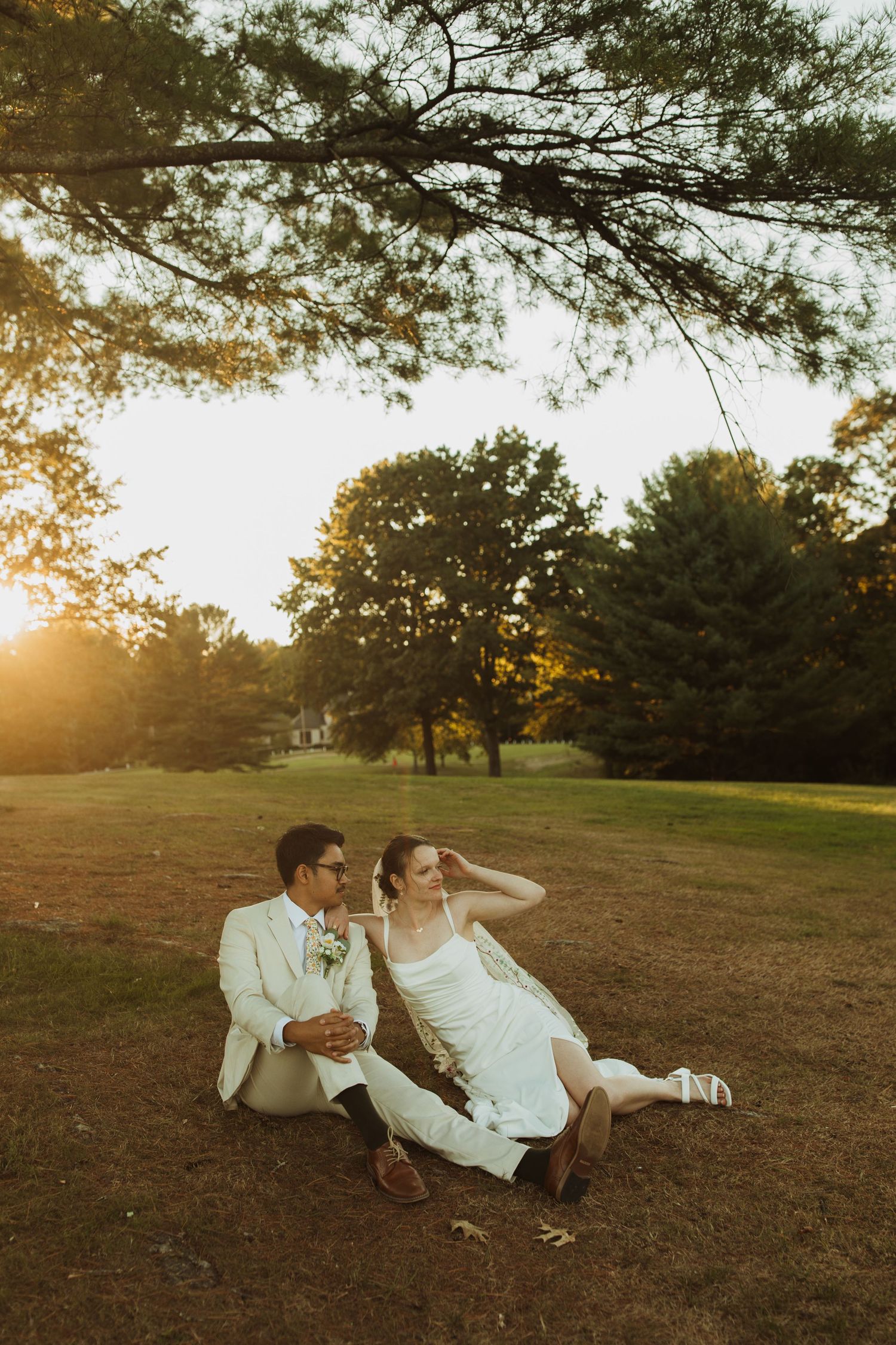 Couple relaxes on grass under pine trees during golden hour sunset.