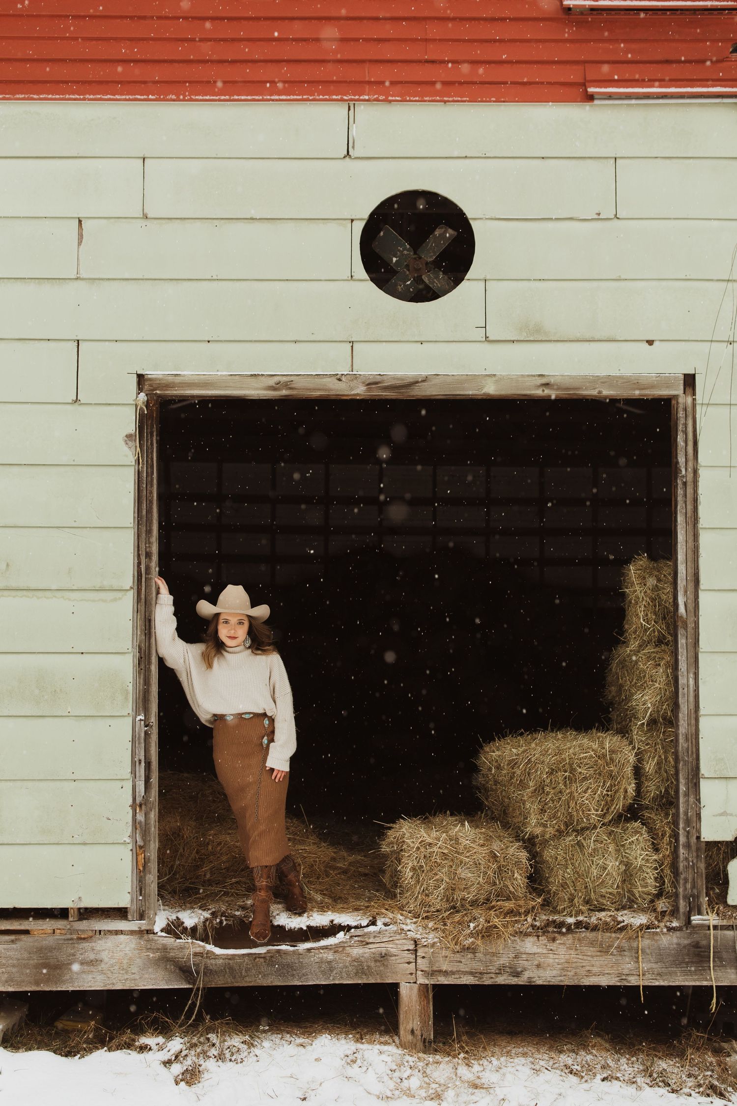 A rustic barn scene with hay bales and white wooden walls in winter.
