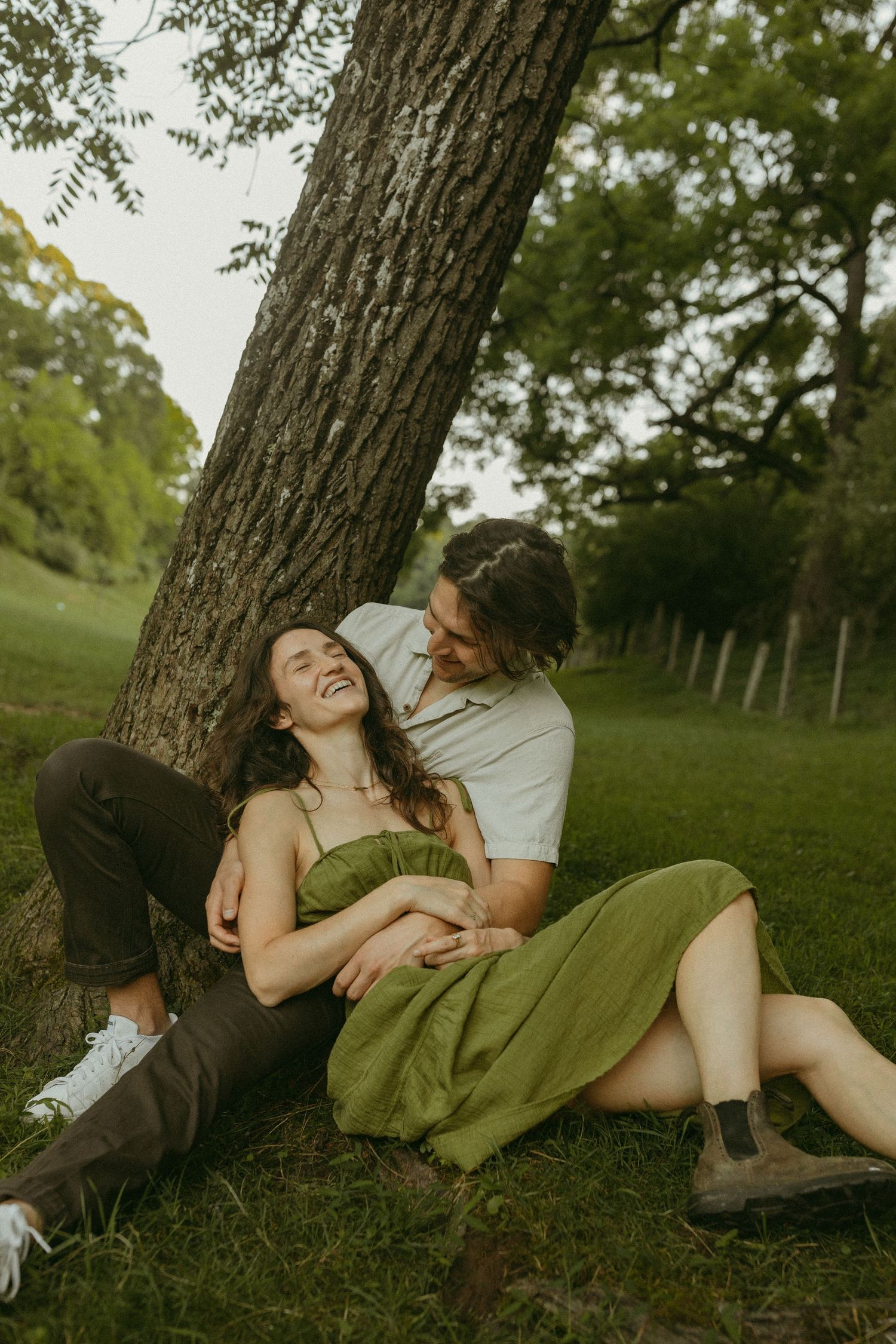 A tender moment shared between two people resting against a tree trunk in dappled sunlight.