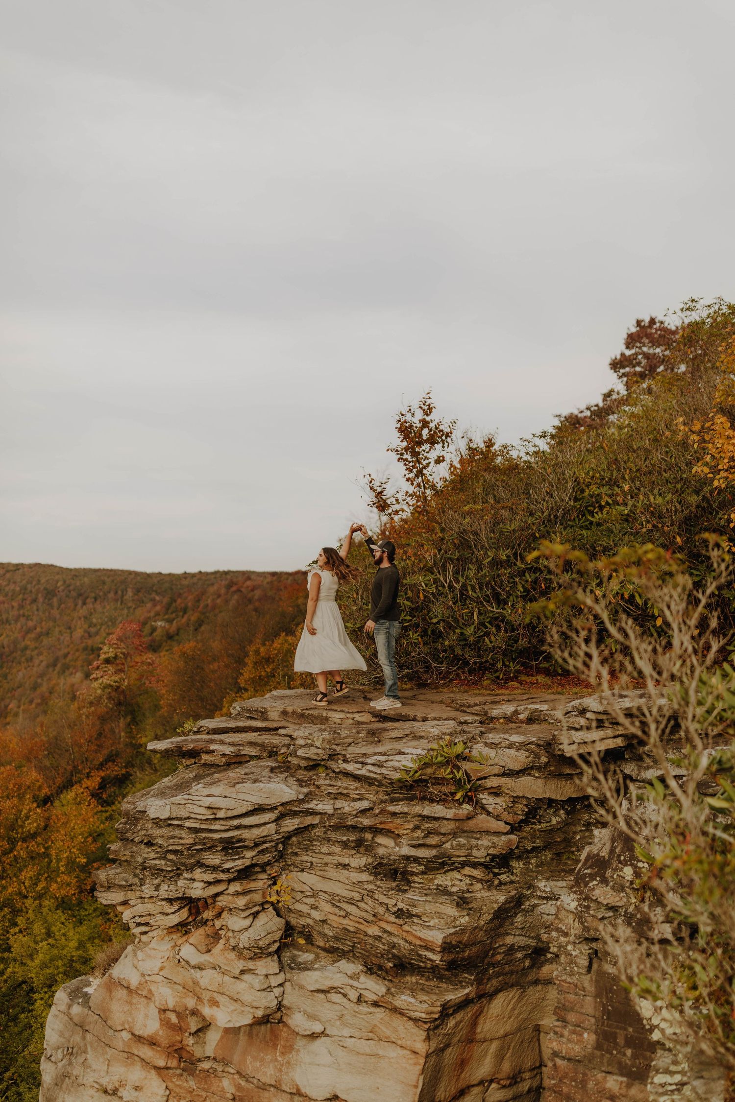 A couple stands on a rocky cliff overlooking a vast autumn valley at lindy point in blackwater falls sate park