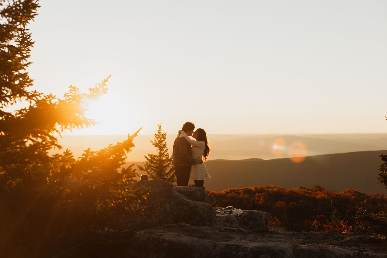 A couple's silhouette against a mountainous landscape during sunset.