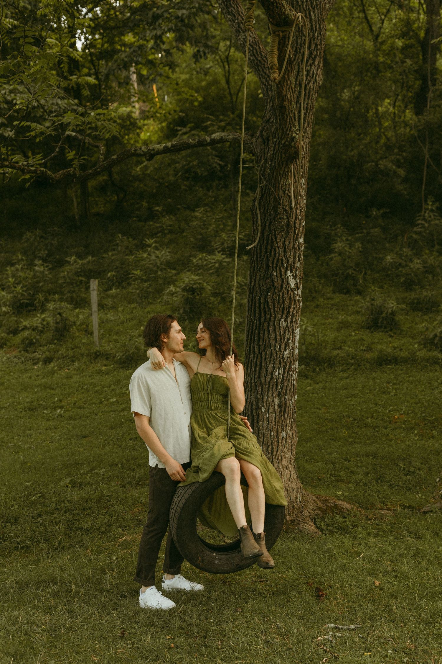 A romantic couple shares an intimate moment by a tree in a lush green park setting during golden hour.