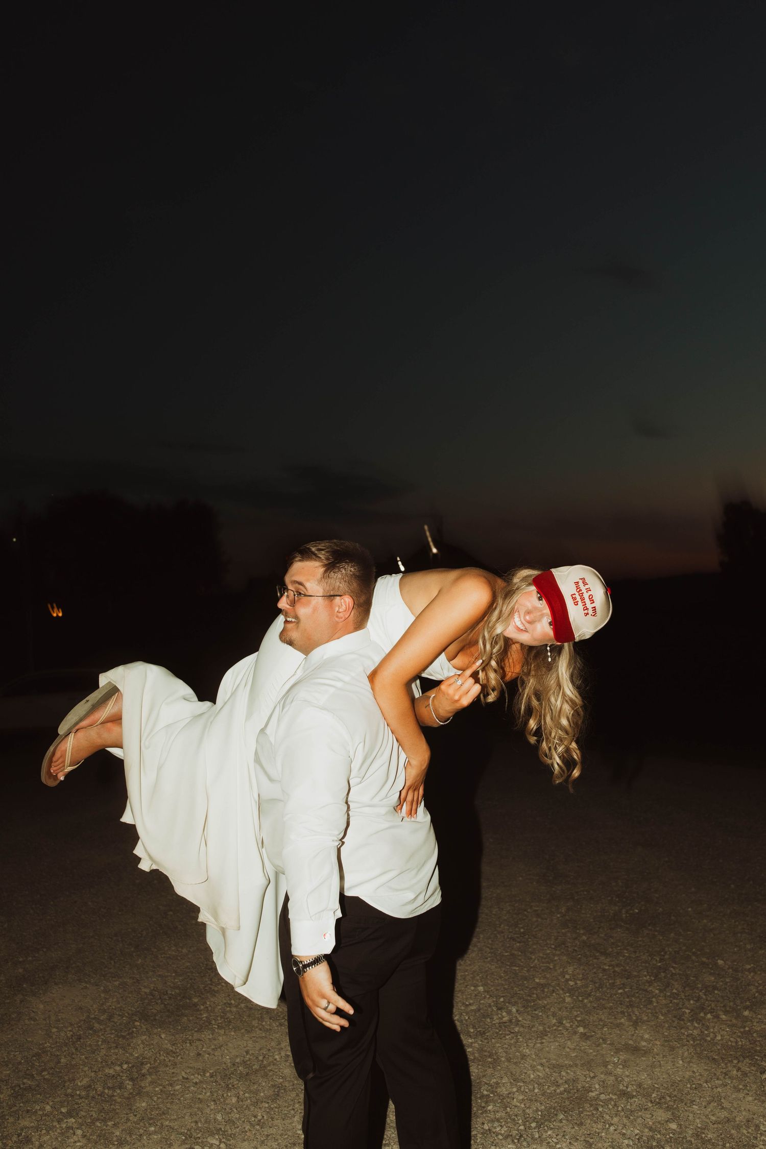 A playful moment captured as a couple in white attire poses during an evening celebration.