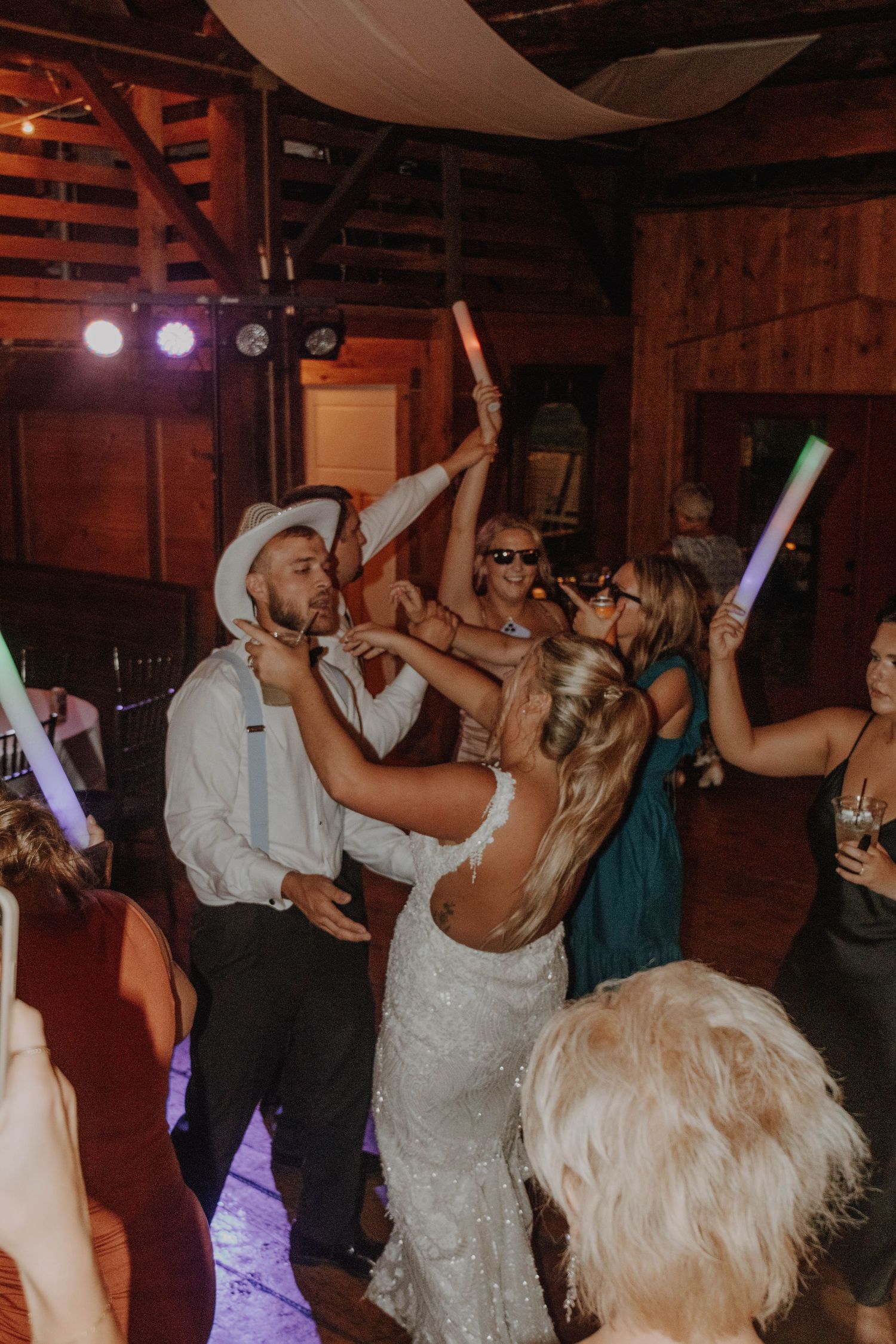 Wedding reception dance party in rustic barn with colorful glow sticks.