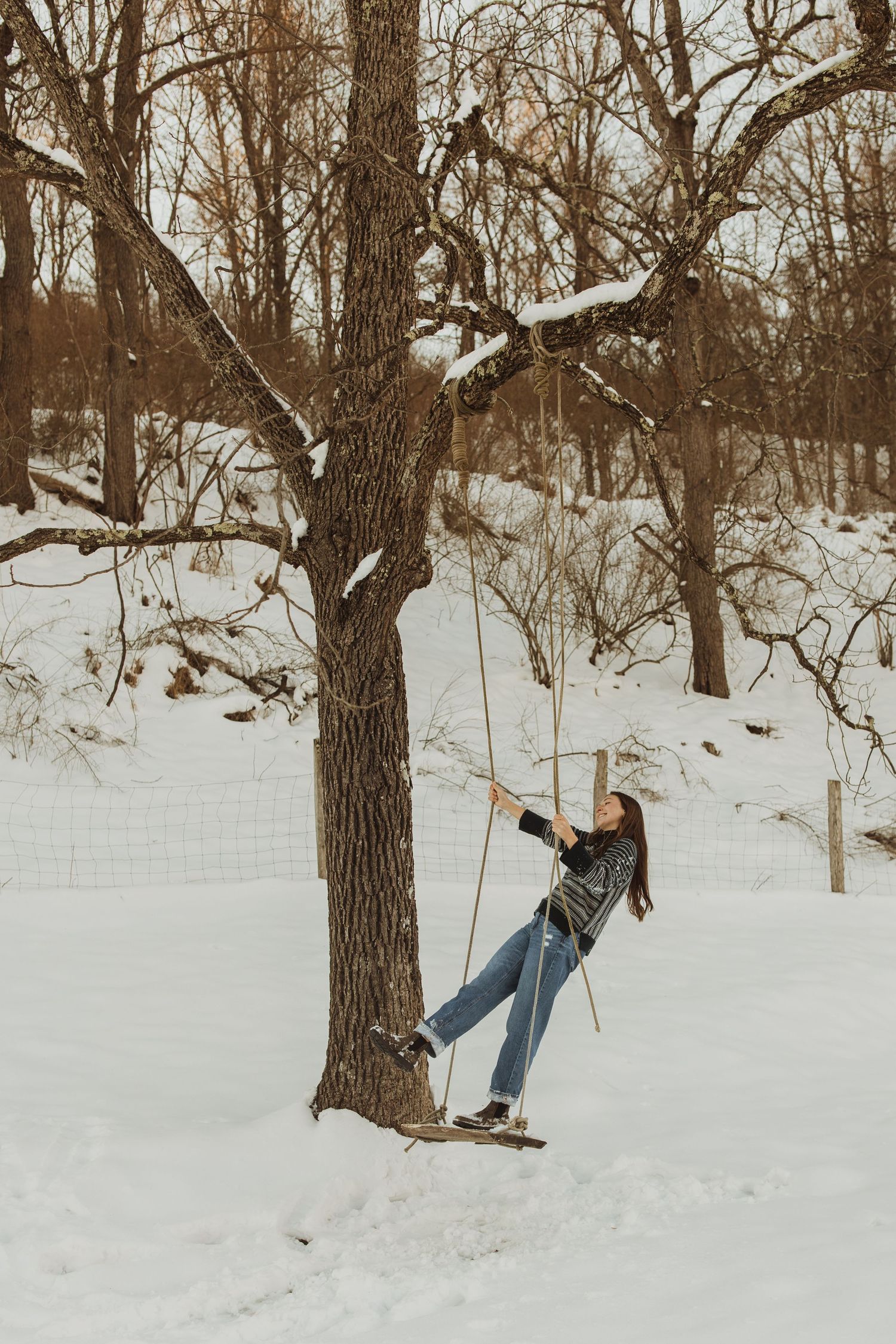 Person swinging on a rope from a tree branch in a snowy winter forest setting.