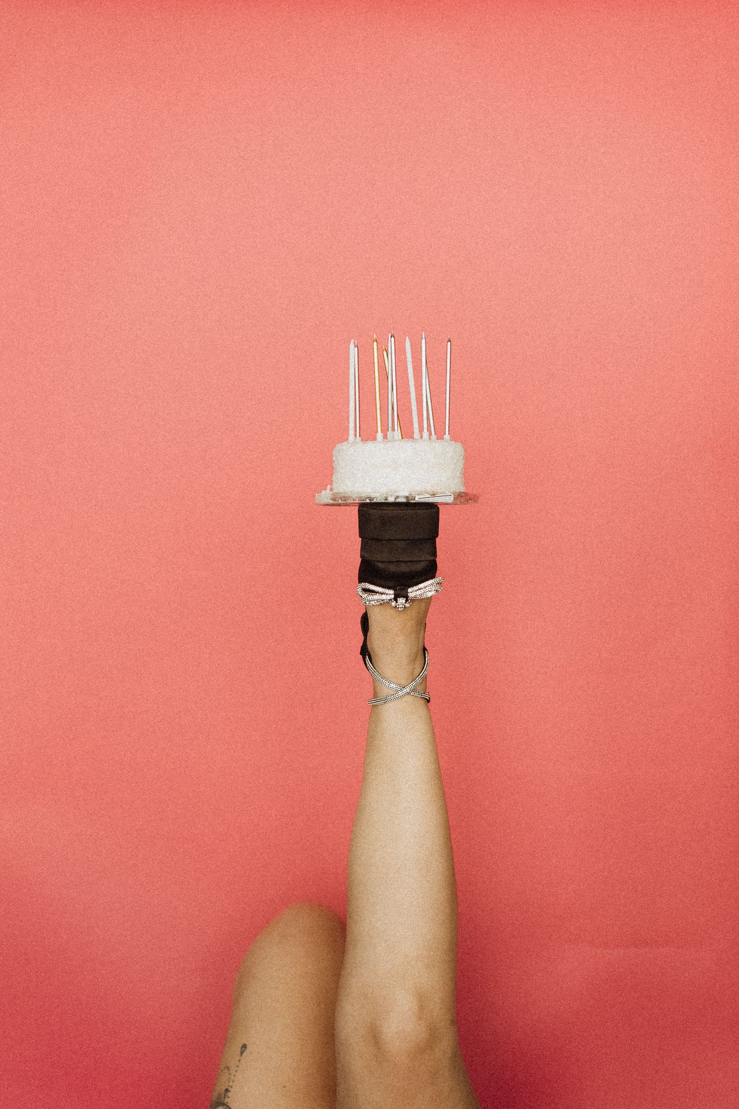 Hand holding small white birthday cake with candles against coral pink background. birthday photoshoot