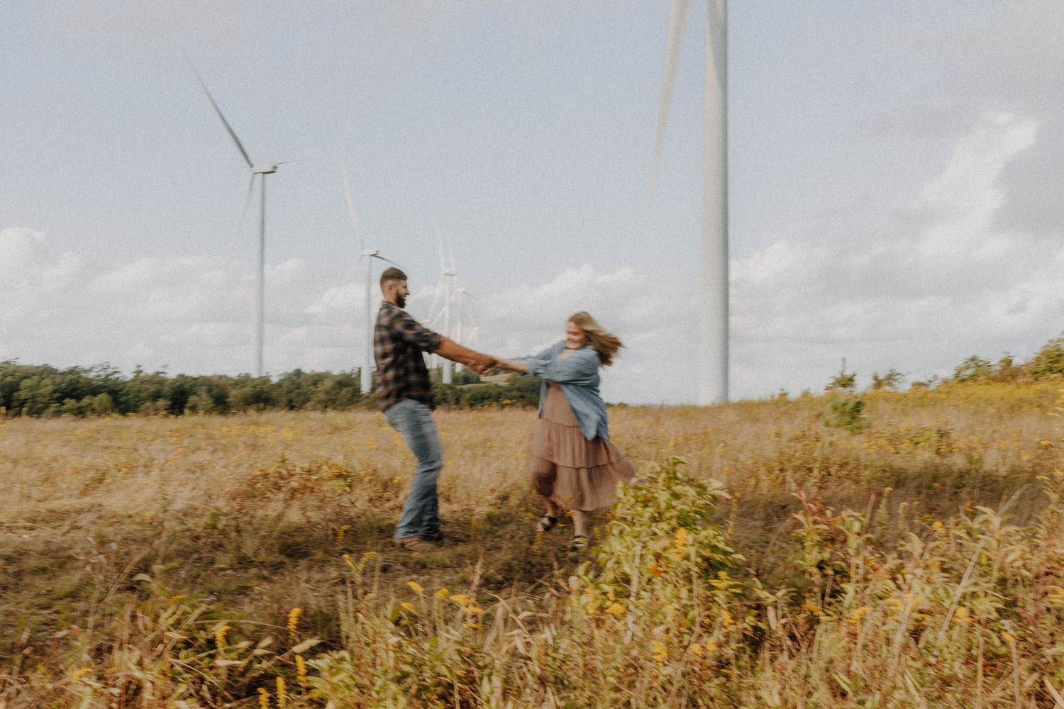 Couple dancing together in field with wind turbines in background.