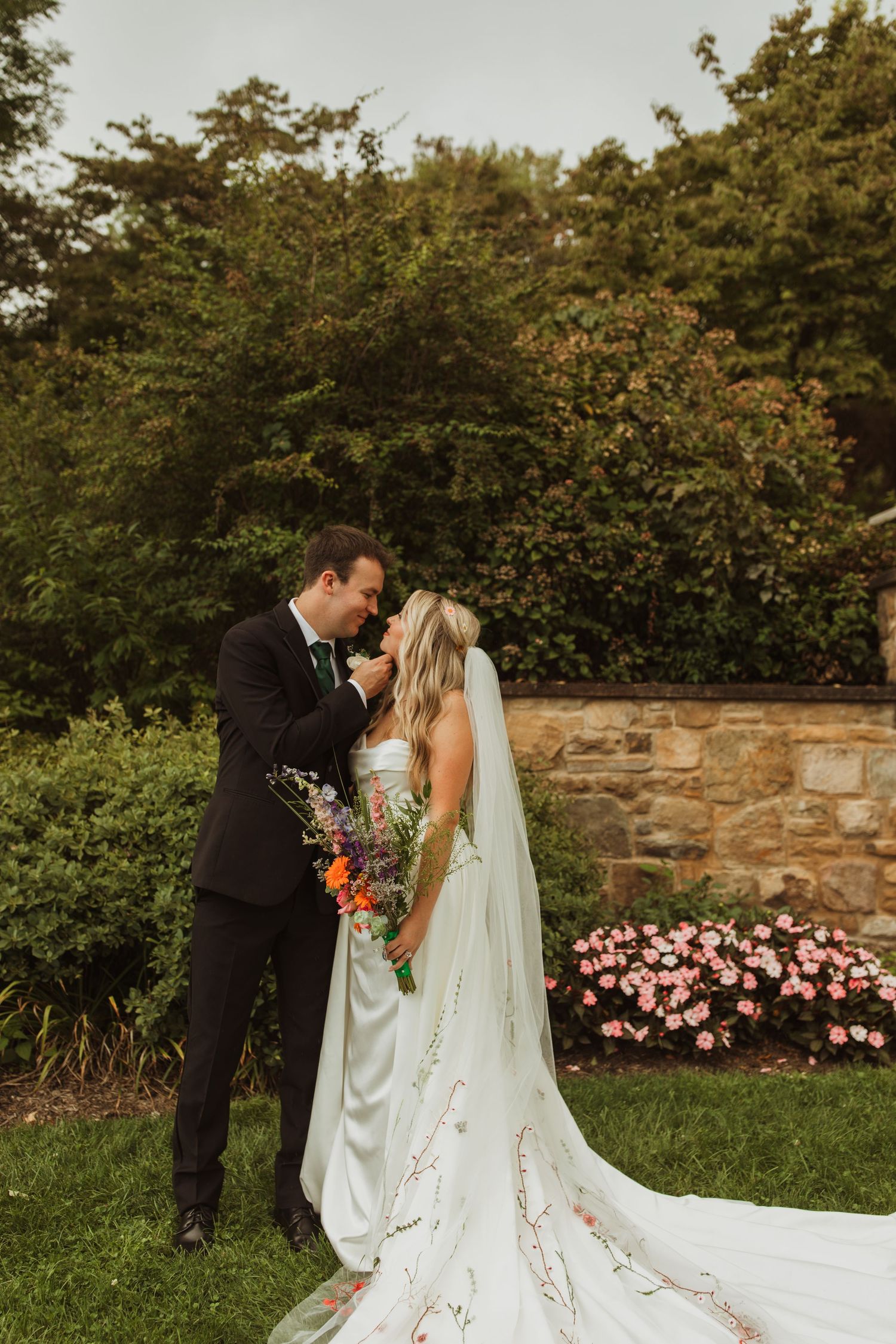 Romantic wedding portrait against a stone wall and pink flowers with a flowing white dress train.