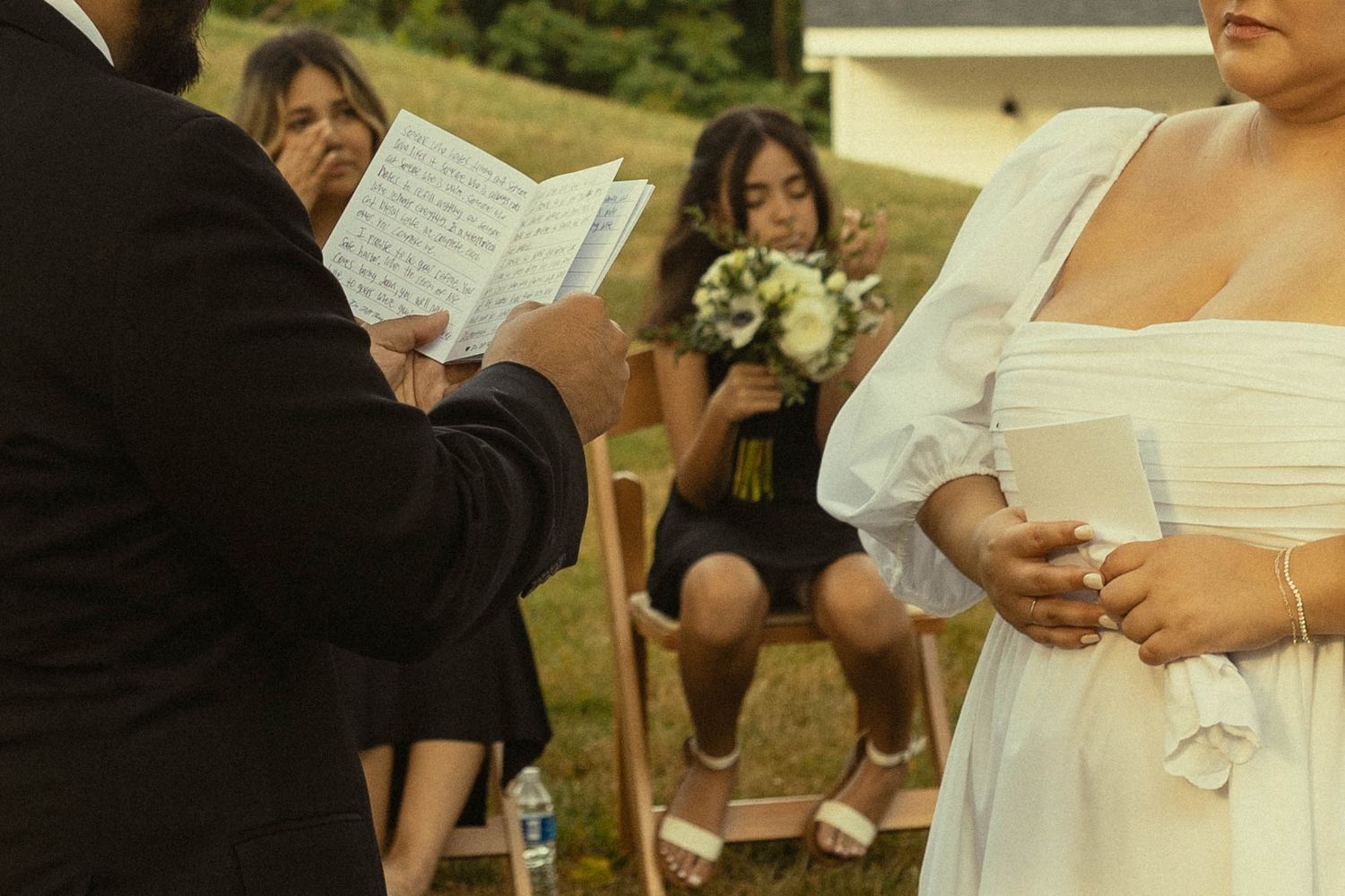 Wedding ceremony in progress showing vow exchange with attendants seated nearby.
