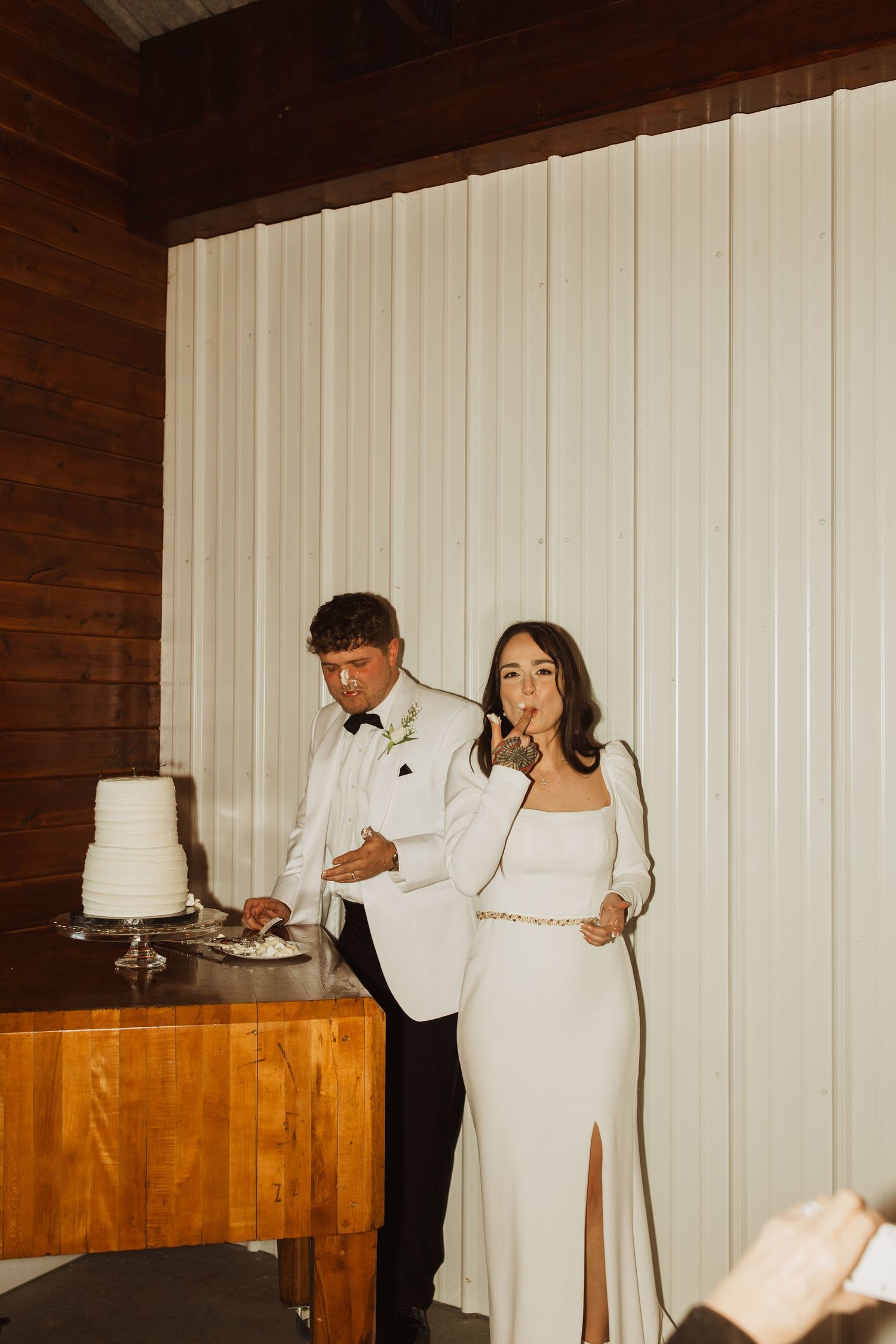 A couple in formal attire cutting their elegant white wedding cake together at the reception.