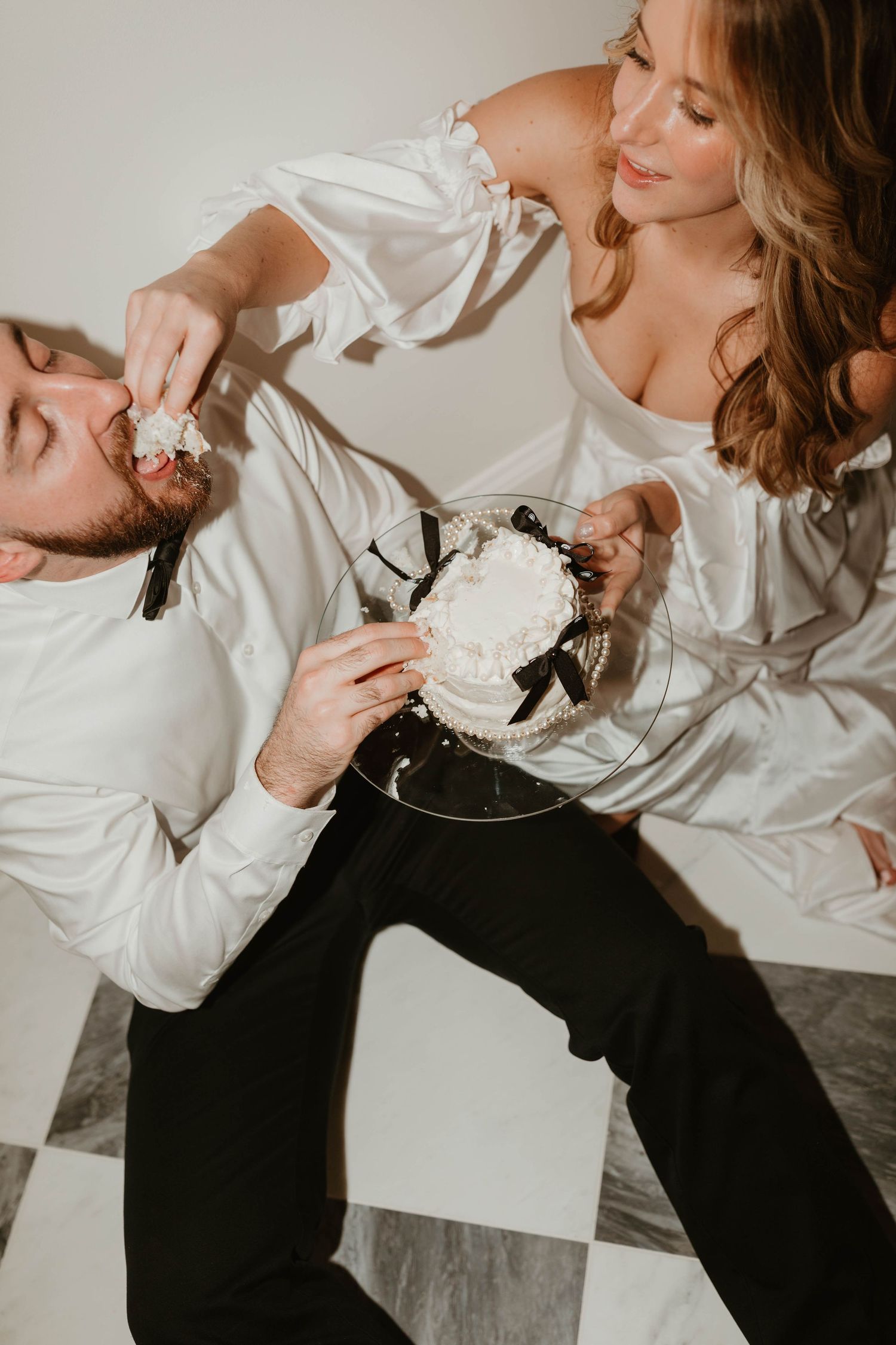 A playful moment shared while eating wedding cake in intimate indoor setting.