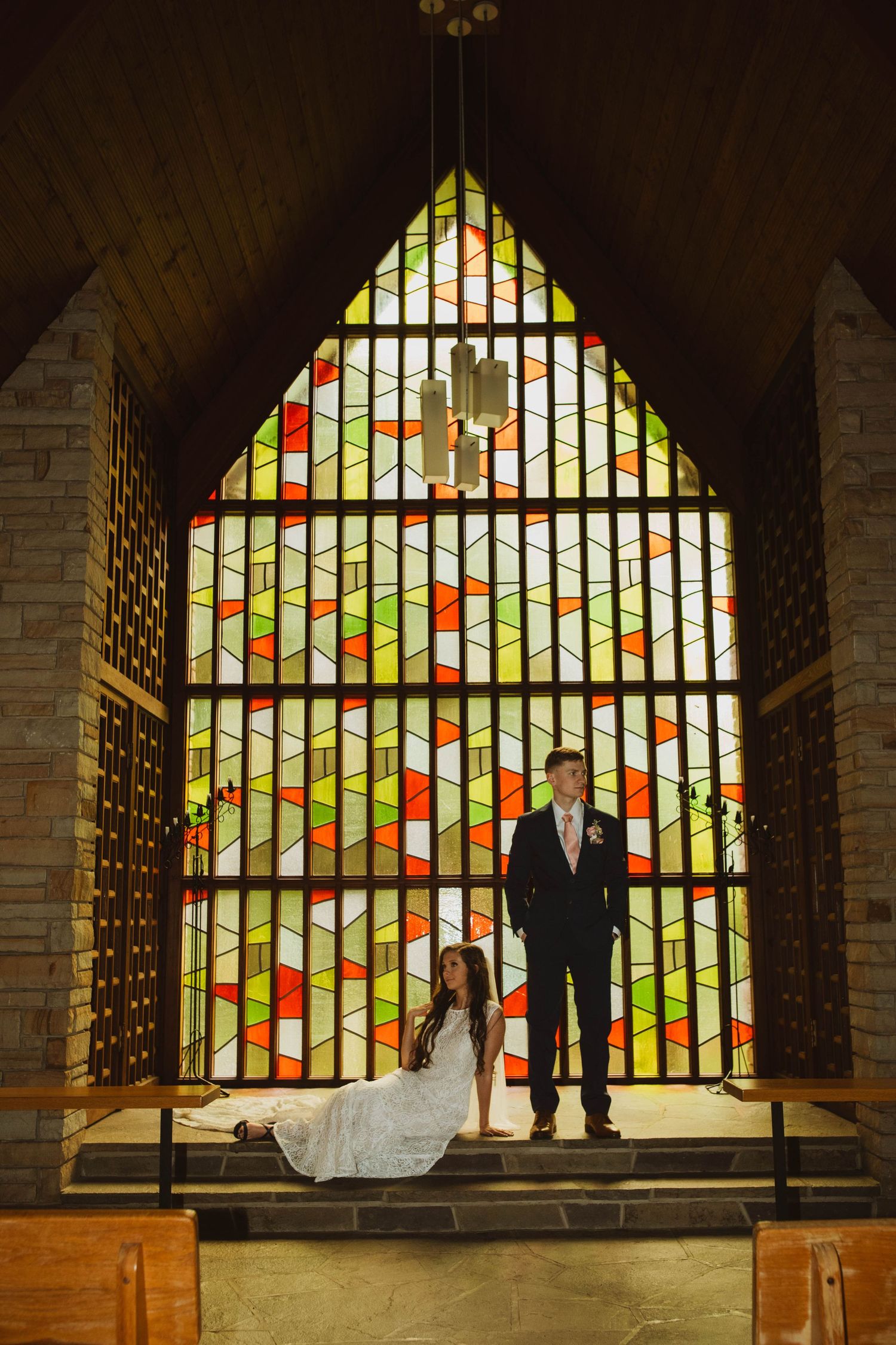A dramatic silhouette of newlyweds against a colorful stained glass window in a chapel.
