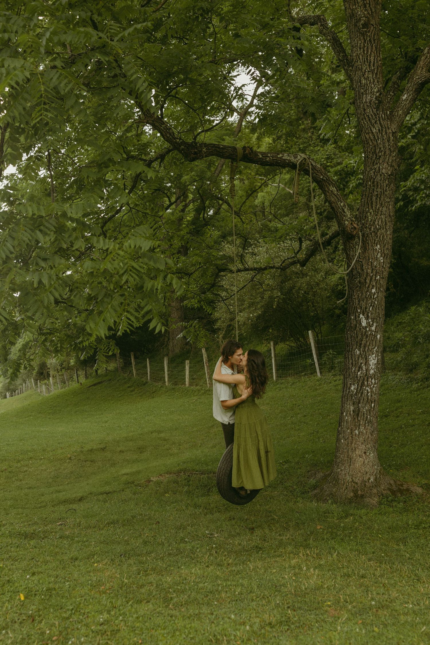 A romantic embrace captured under a large tree in a serene park setting.