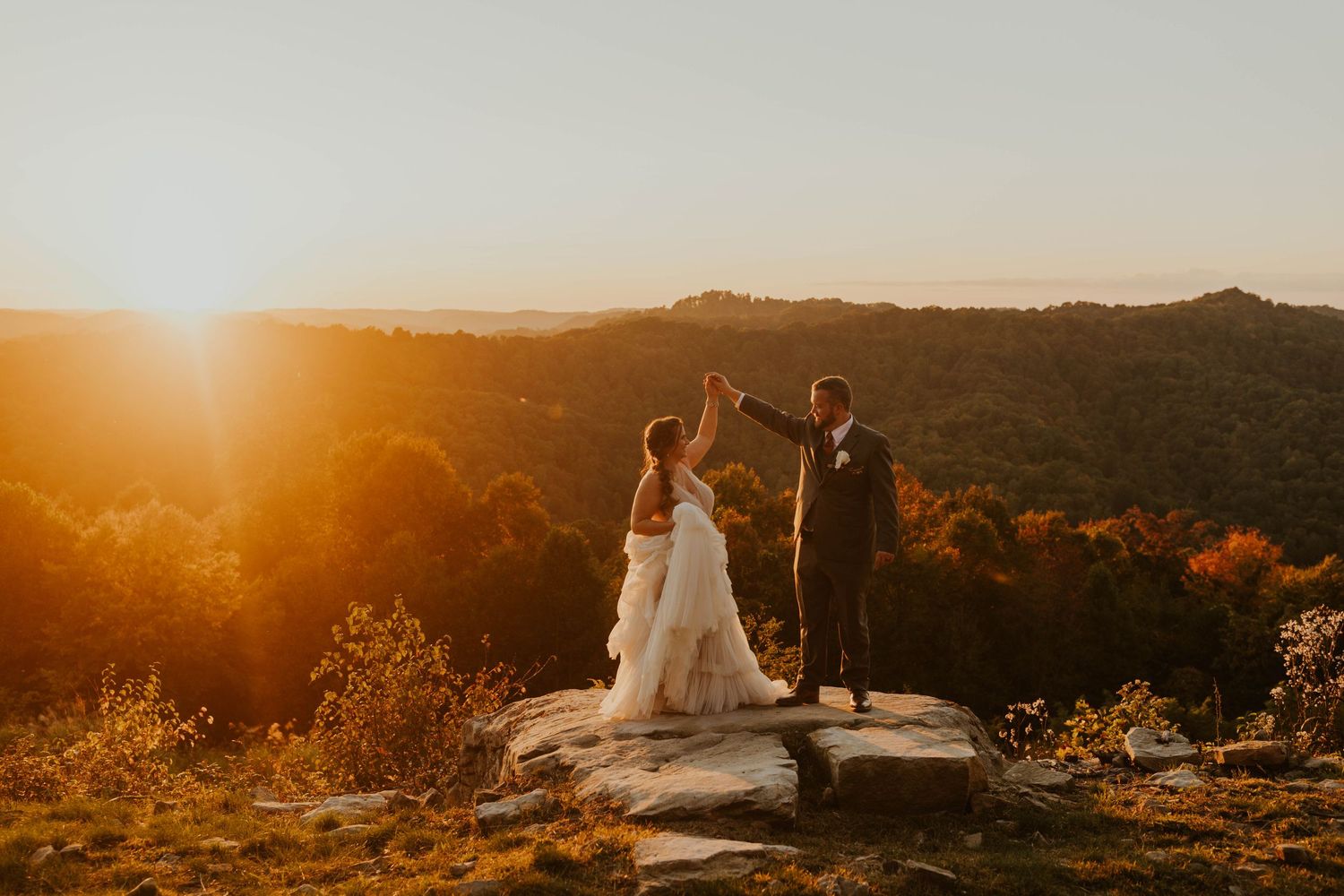 Couple sharing a joyful dance on a rocky mountain peak at sunset.