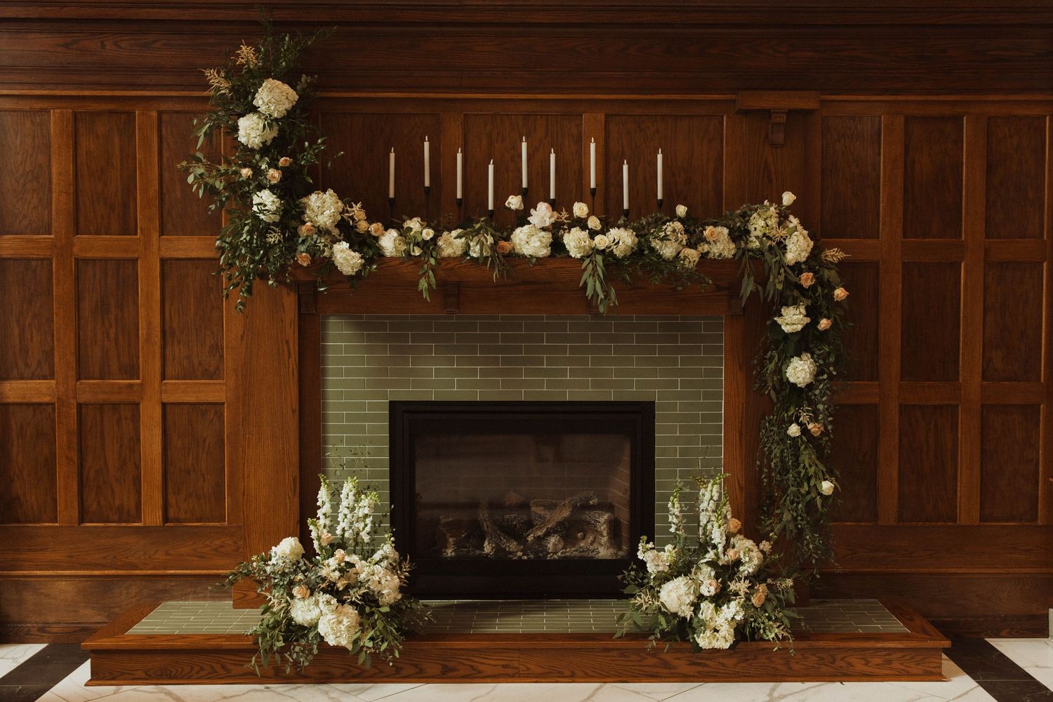 Fireplace decorated with white floral garland and greenery for wedding ceremony.