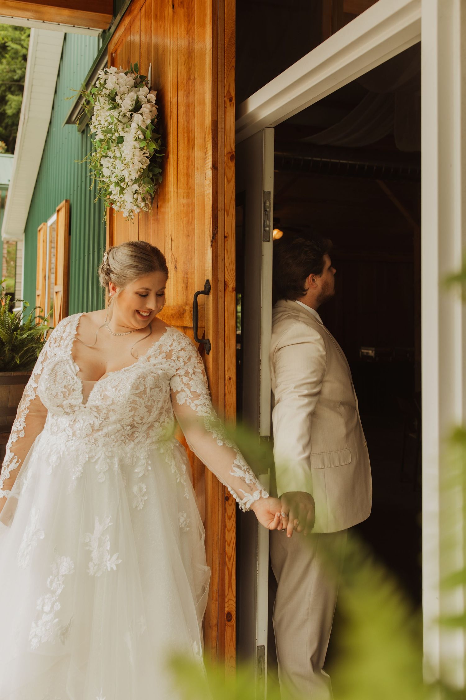 Wedding couple shares first look moment while separated by rustic wooden doorway.