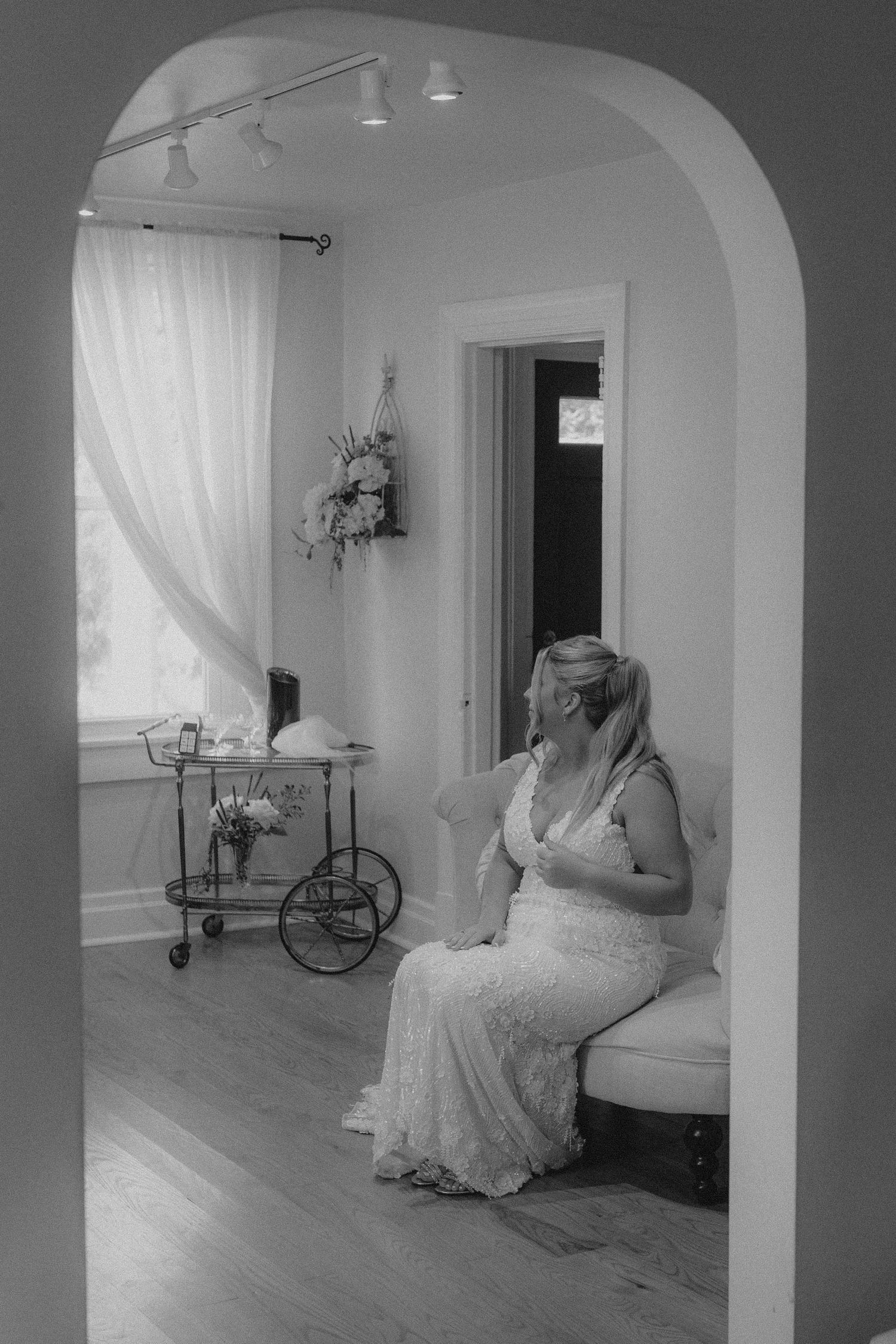 Monochrome image of bride resting in white chair during wedding preparation.
