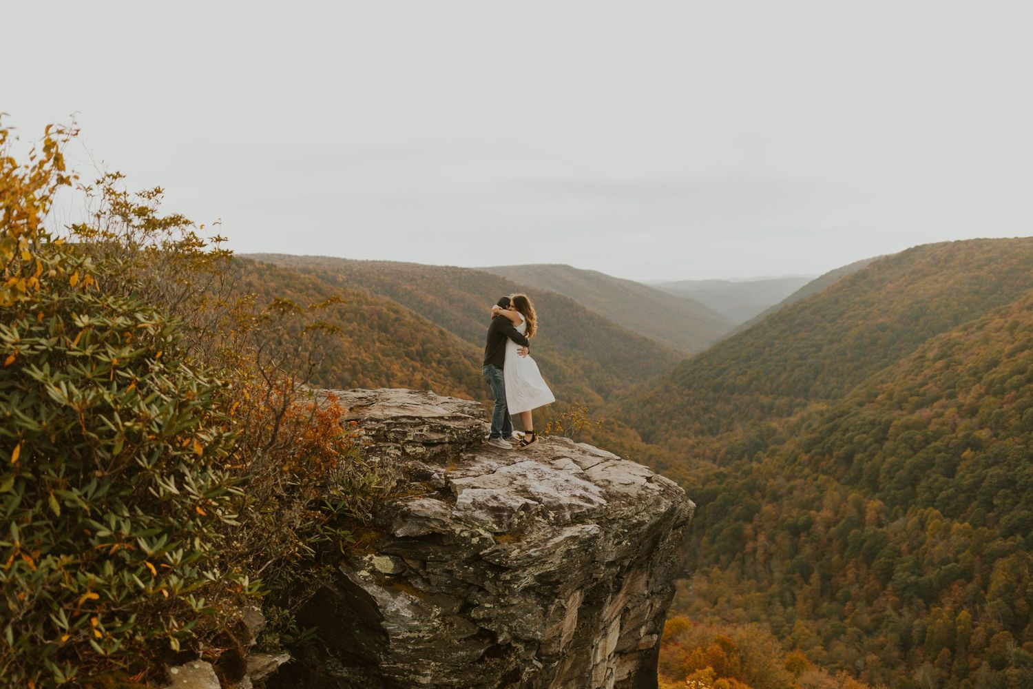 A couple stands on a dramatic rocky cliff overlook during autumn/fall,  at lindy point in blackwater falls state park