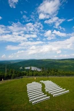 White ceremony chairs arranged on a hilltop lawn with mountain views and blue skies.