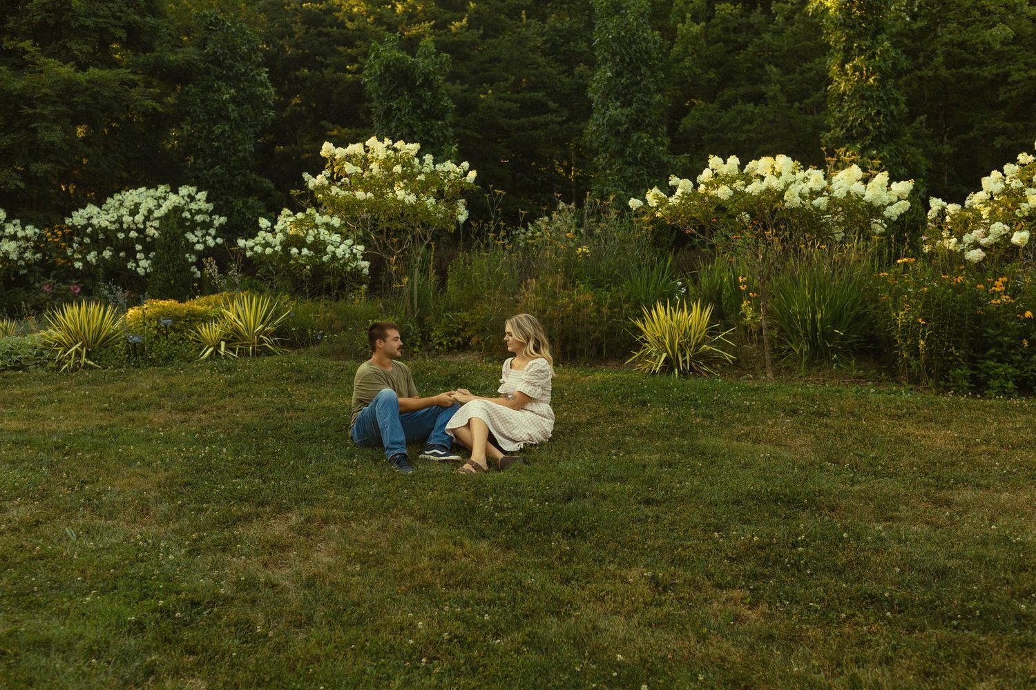 Couple sitting together on grass with blooming flowers in garden background.
