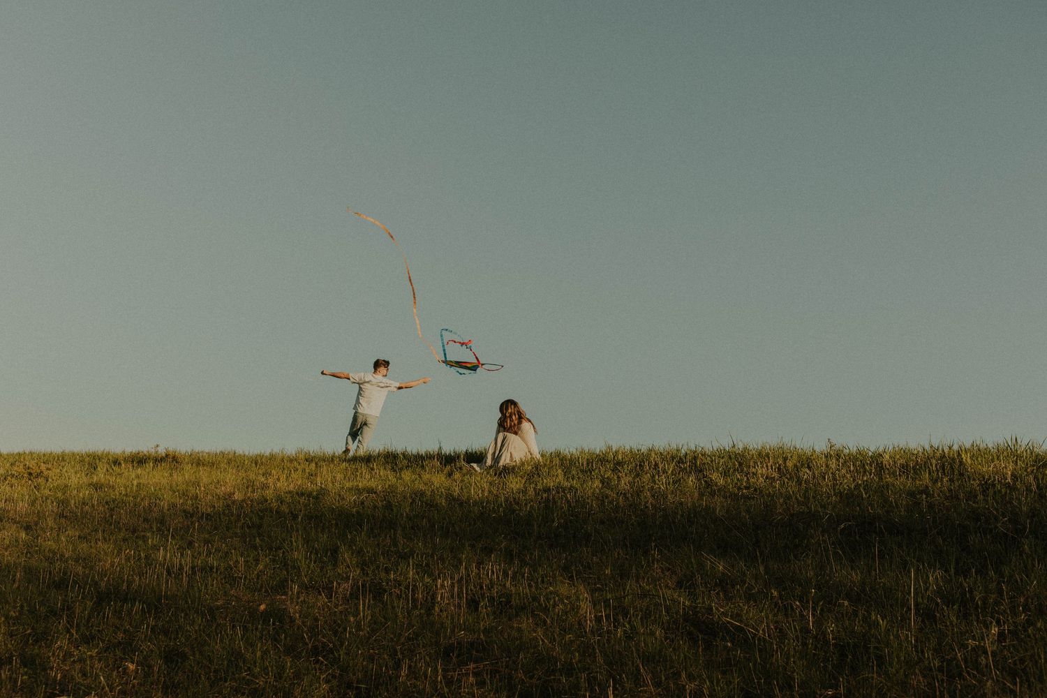 Two silhouettes stand on a hilltop against a moody grey sky.