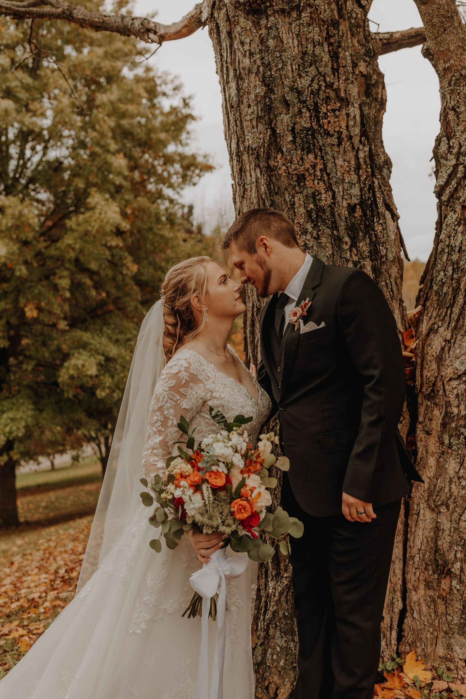 A romantic autumn wedding portrait under a large tree with orange and red florals.
