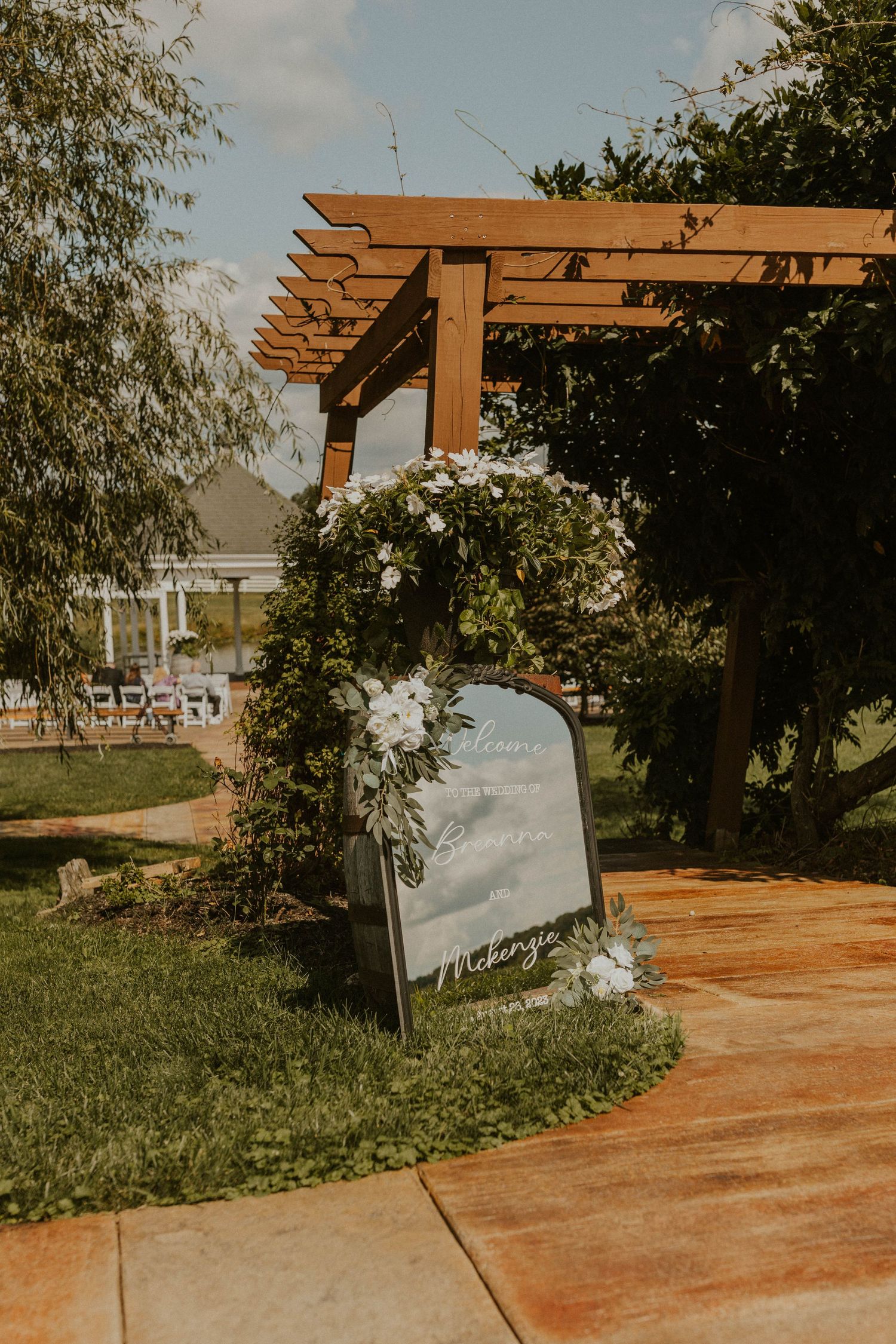 Rustic wooden pergola with white flowers and signage at an outdoor wedding venue entrance.