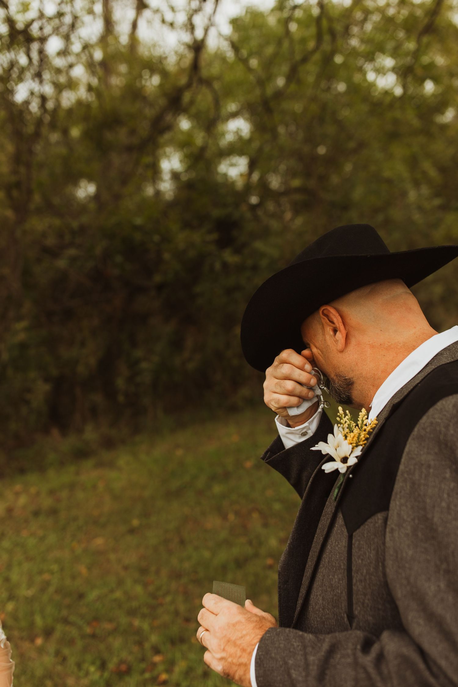 An emotional moment during a wedding ceremony with a person wearing a black cowboy hat wiping away tears.