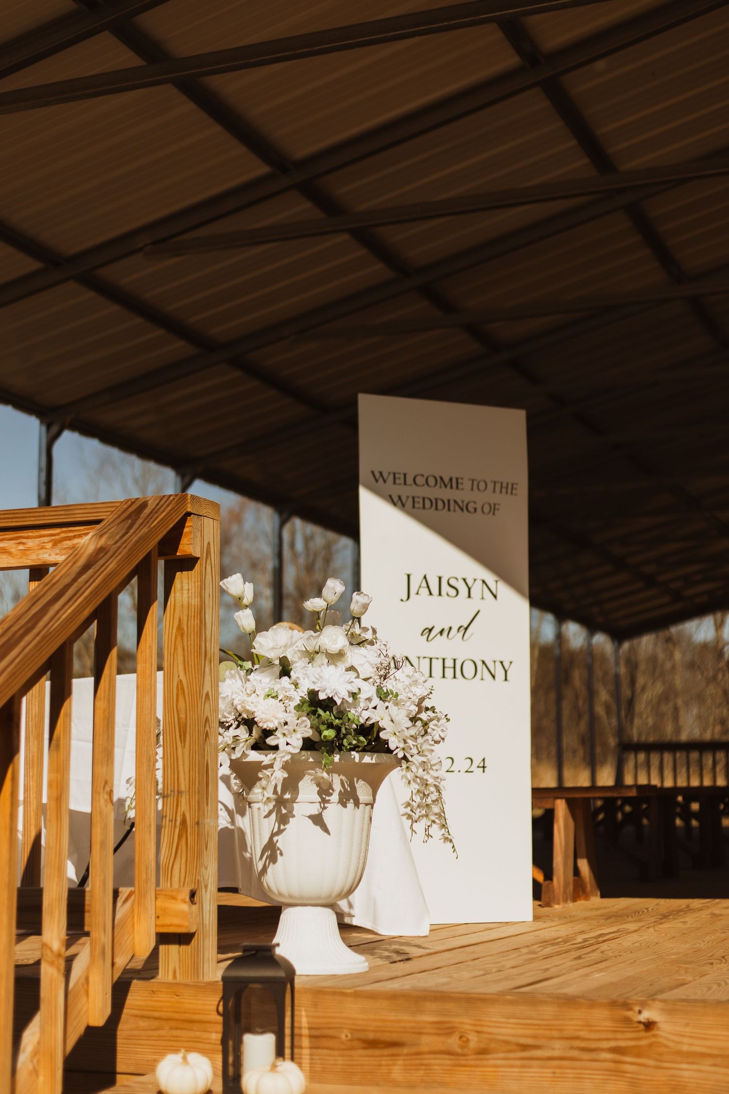 Elegant wedding welcome sign with floral arrangement at rustic outdoor venue.