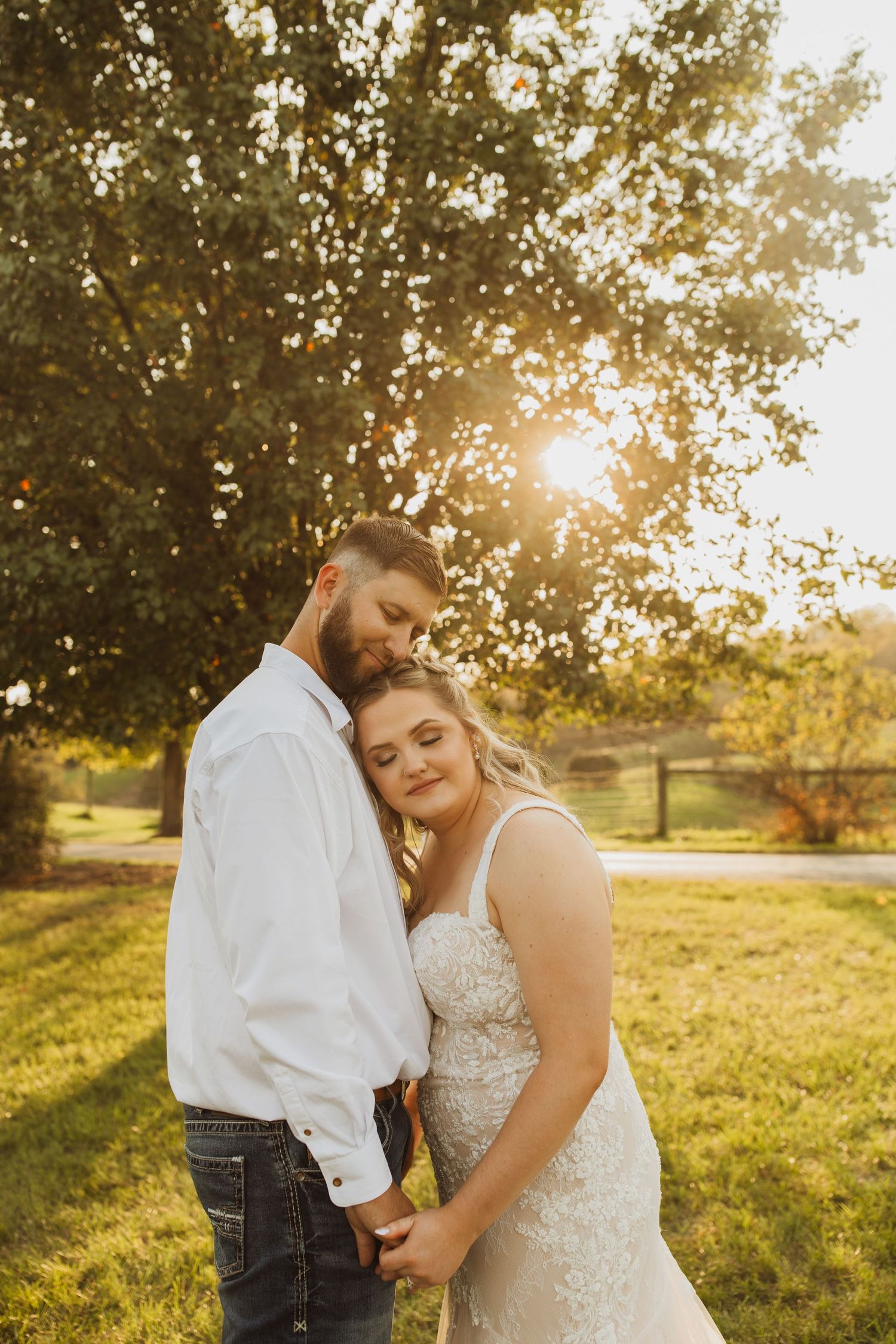 A couple embraces in a sunlit meadow at golden hour while wearing wedding attire.