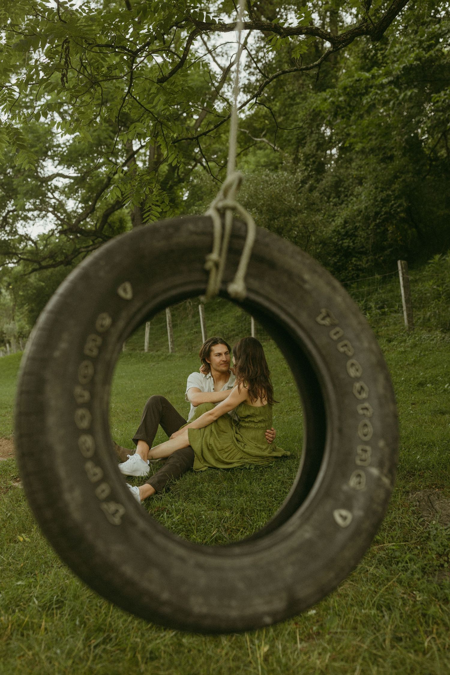 Creative engagement photo framed through tire swing in lush green garden setting.