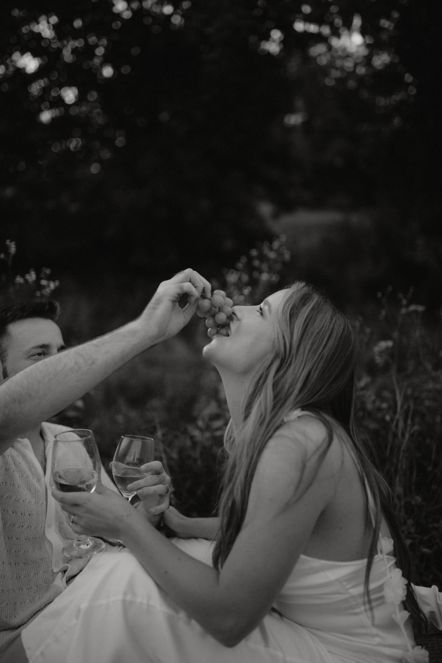 A black and white romantic moment captured during an outdoor wine picnic.