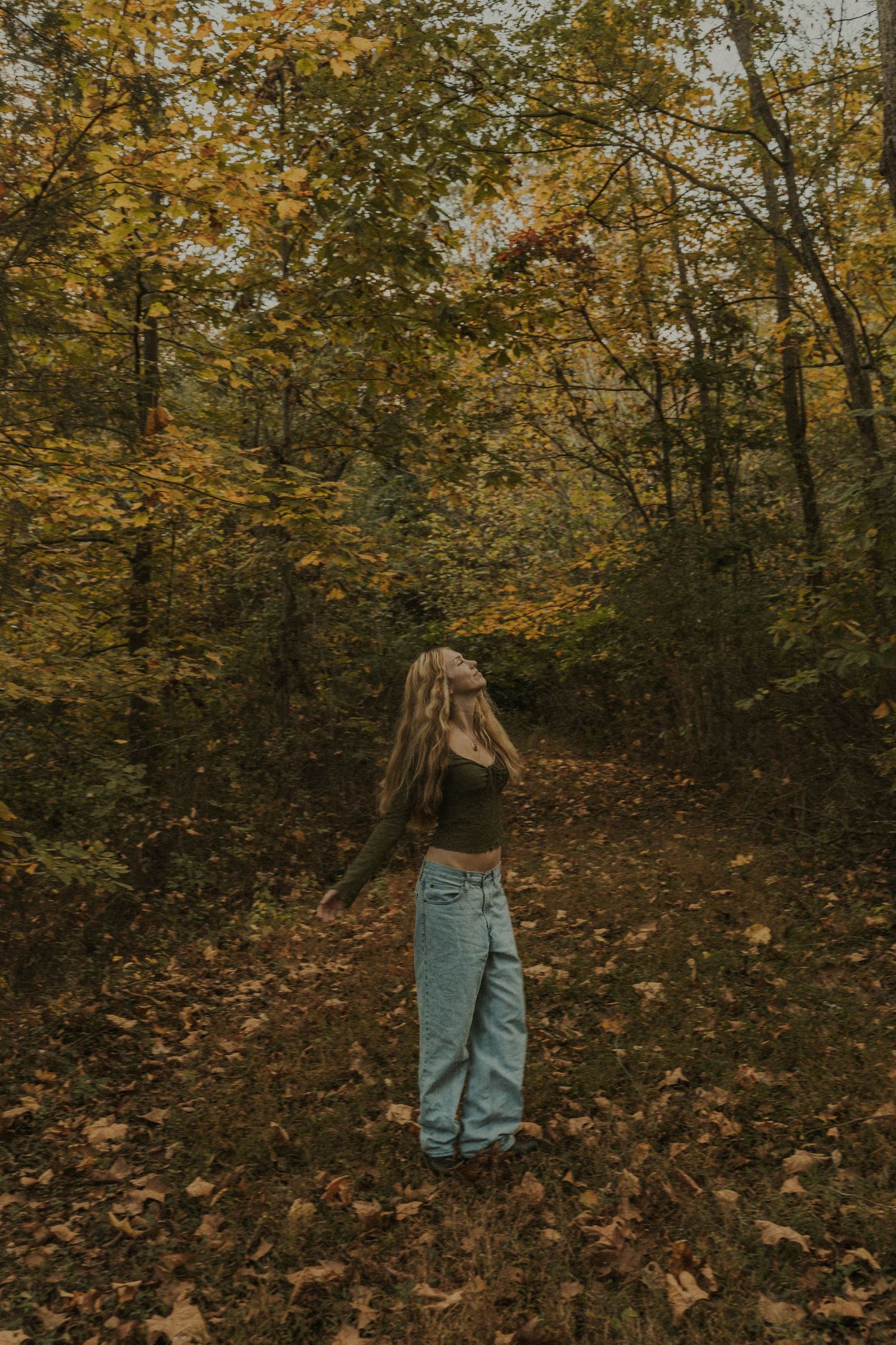 Person walking on leaf-covered trail through golden autumn forest.