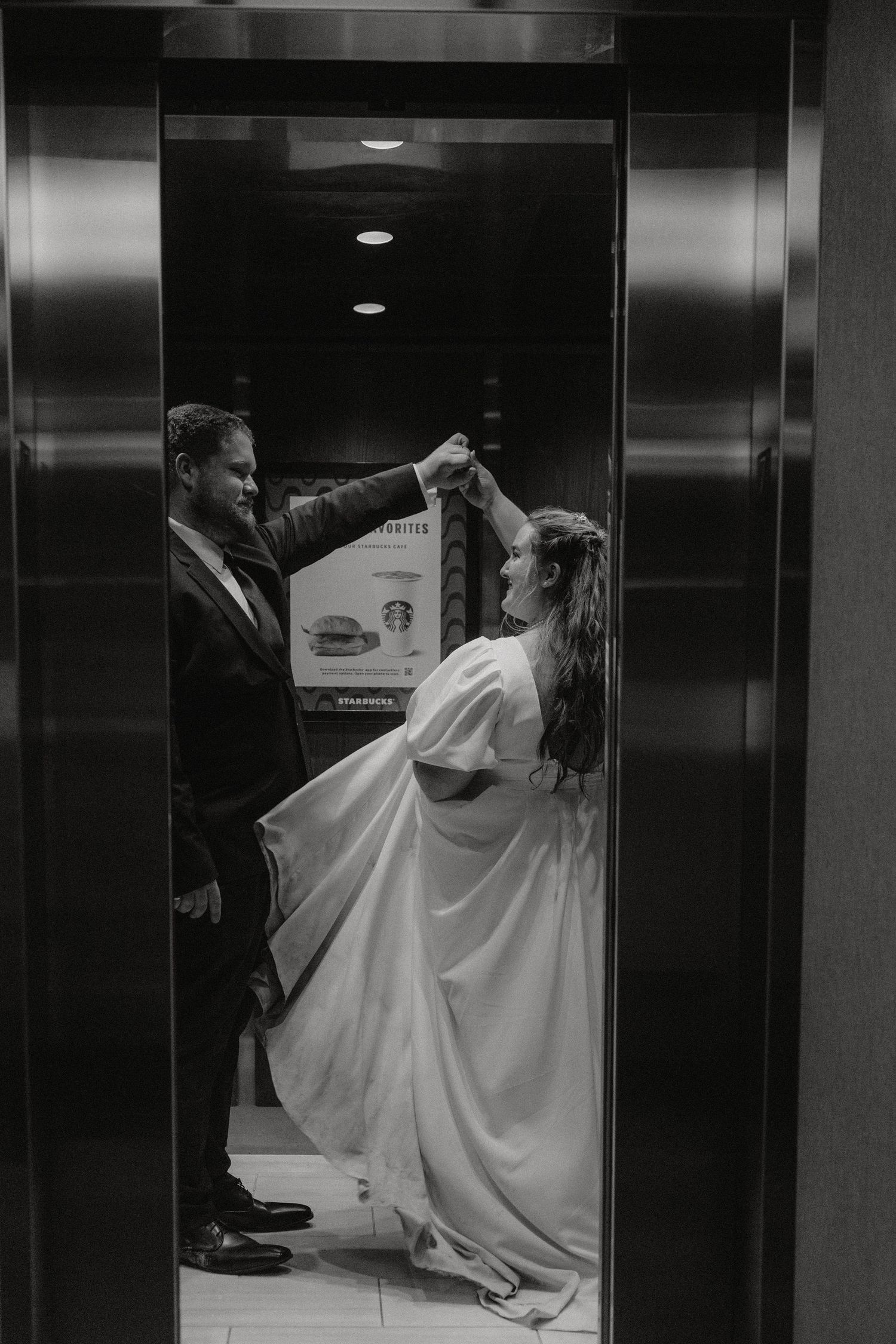 Dancing couple in wedding attire spins gracefully inside a silver elevator.