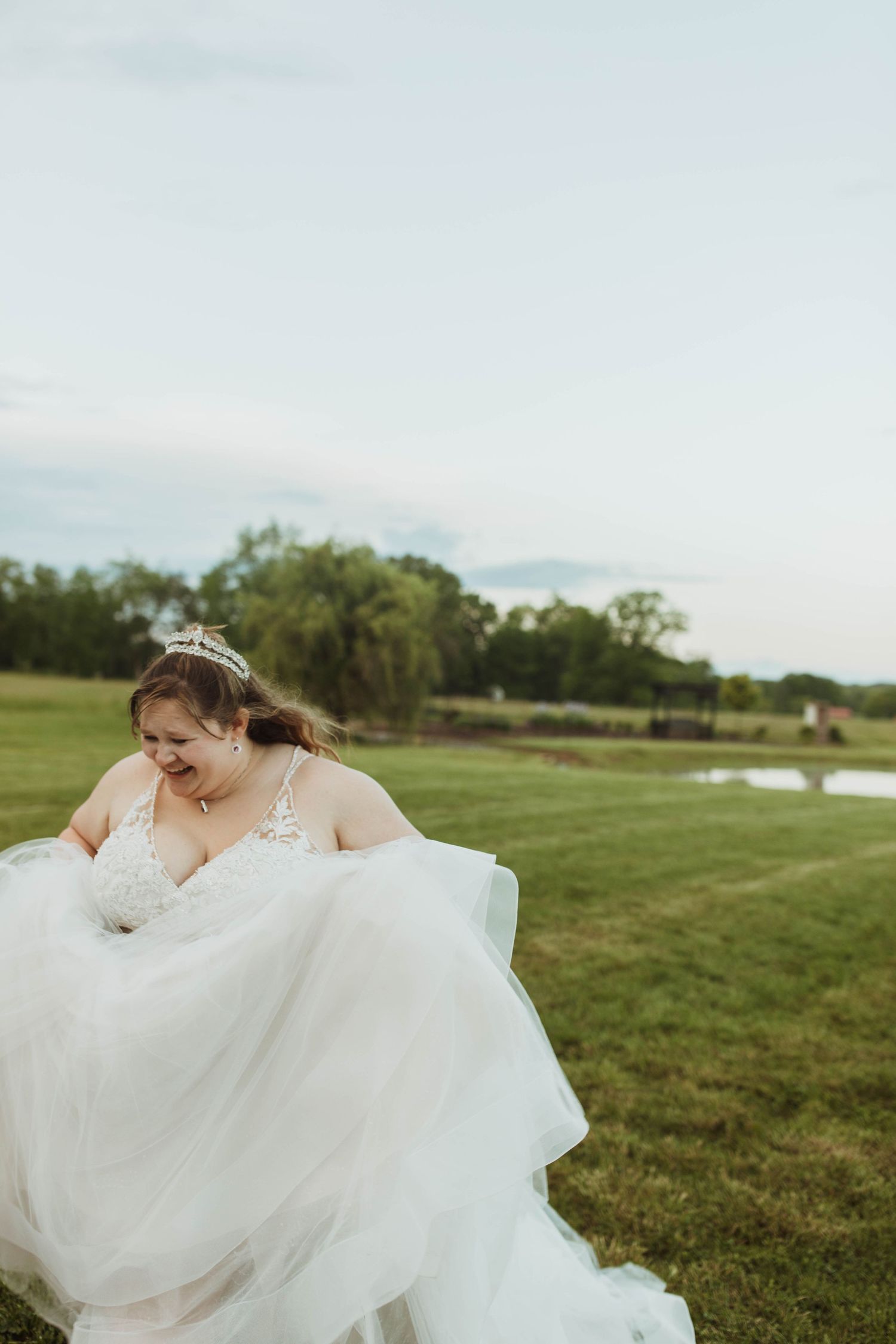 A bride in a flowing white dress twirls joyfully in an open field.