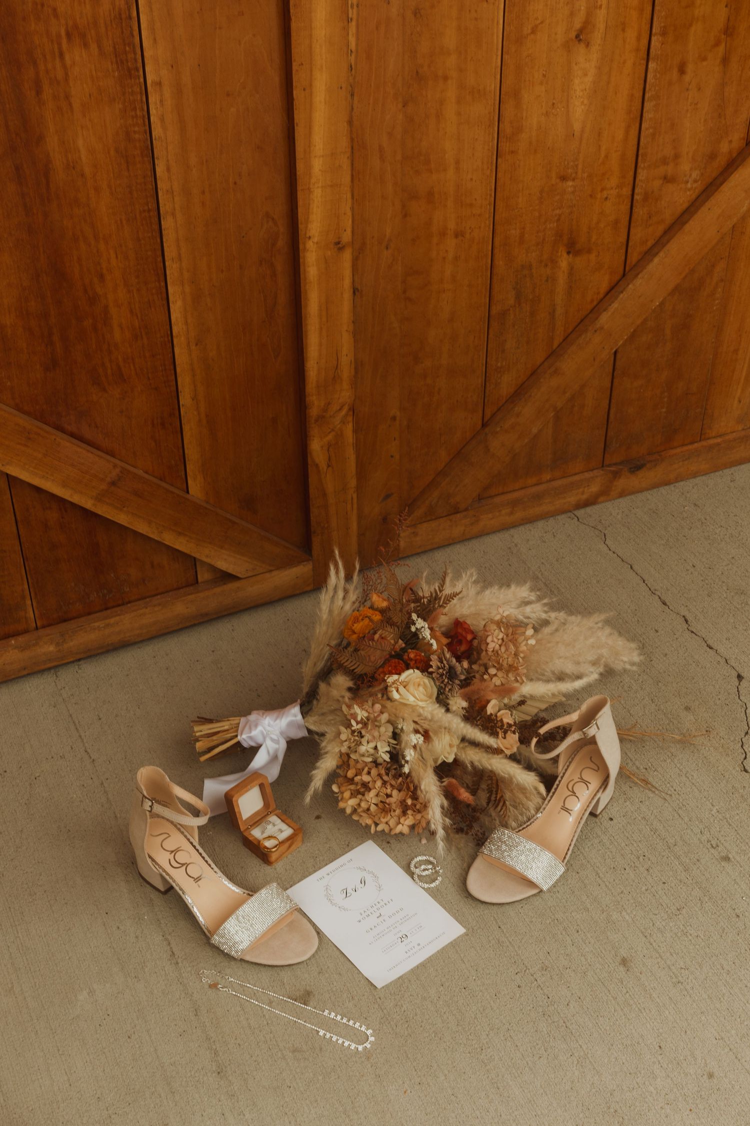 Wedding accessories including beige sandals and dried flower bouquet arranged on floor by wooden door.