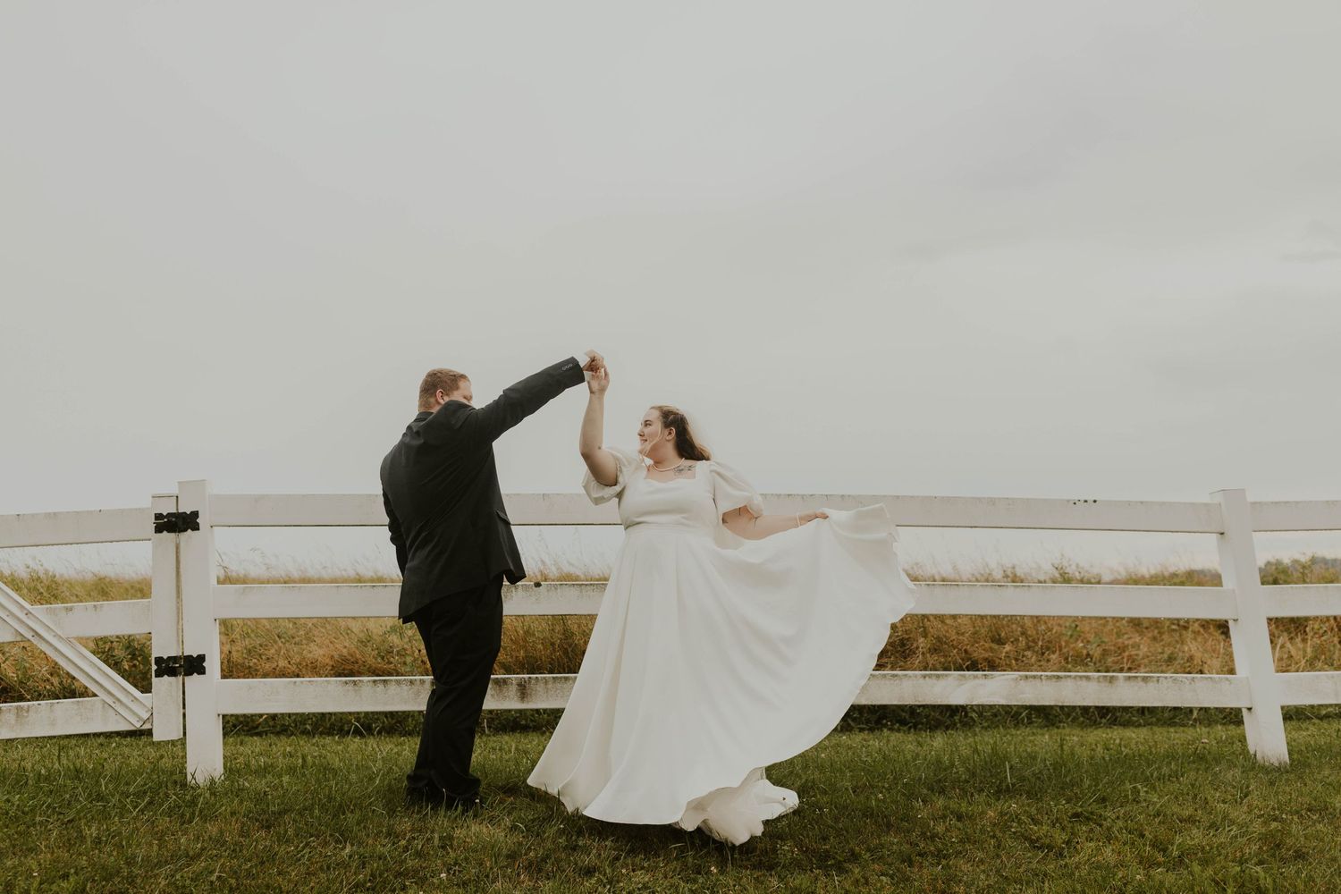 A joyful dancing moment between newlyweds by a white fence.