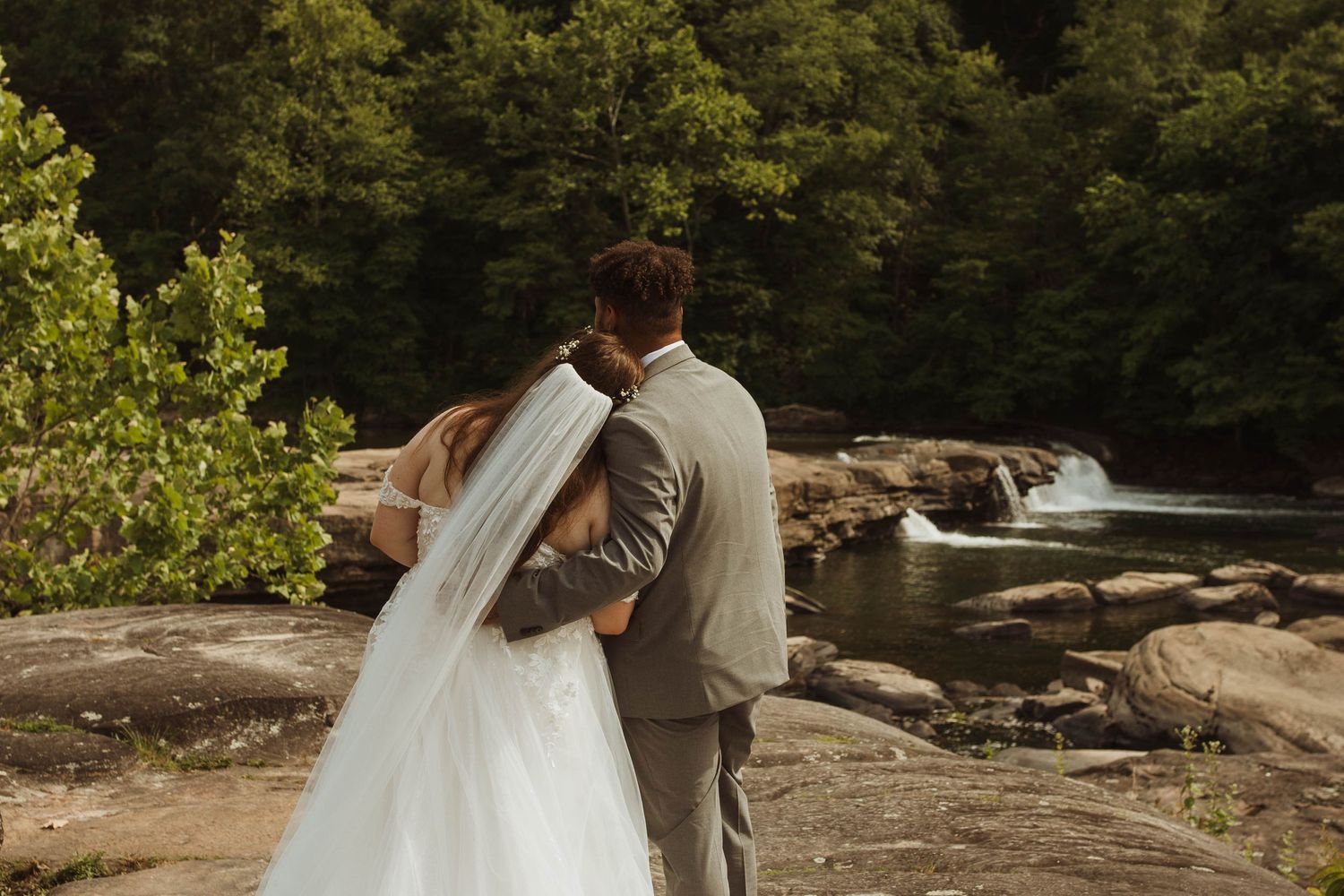 A couple in wedding attire share a romantic moment overlooking a scenic waterfall on their special day at valley falls