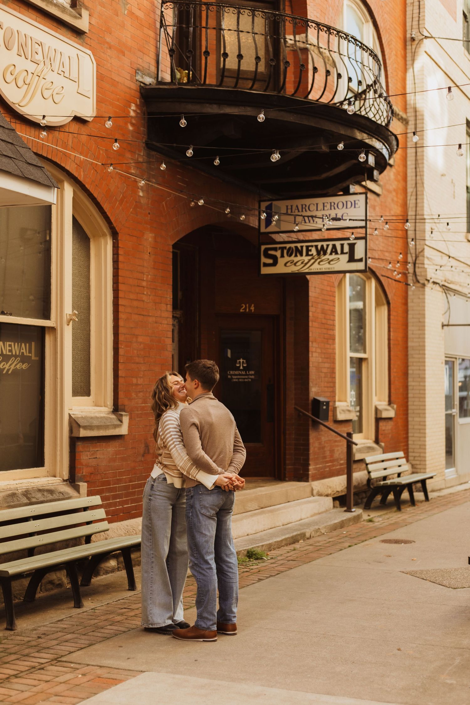 A romantic moment shared between two people outside a brick building with a vintage cafe sign.