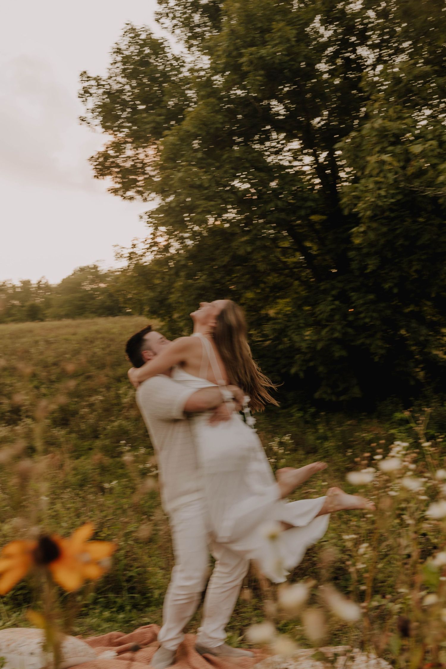 A joyful embrace captured in warm sunset light with wildflowers in the foreground.