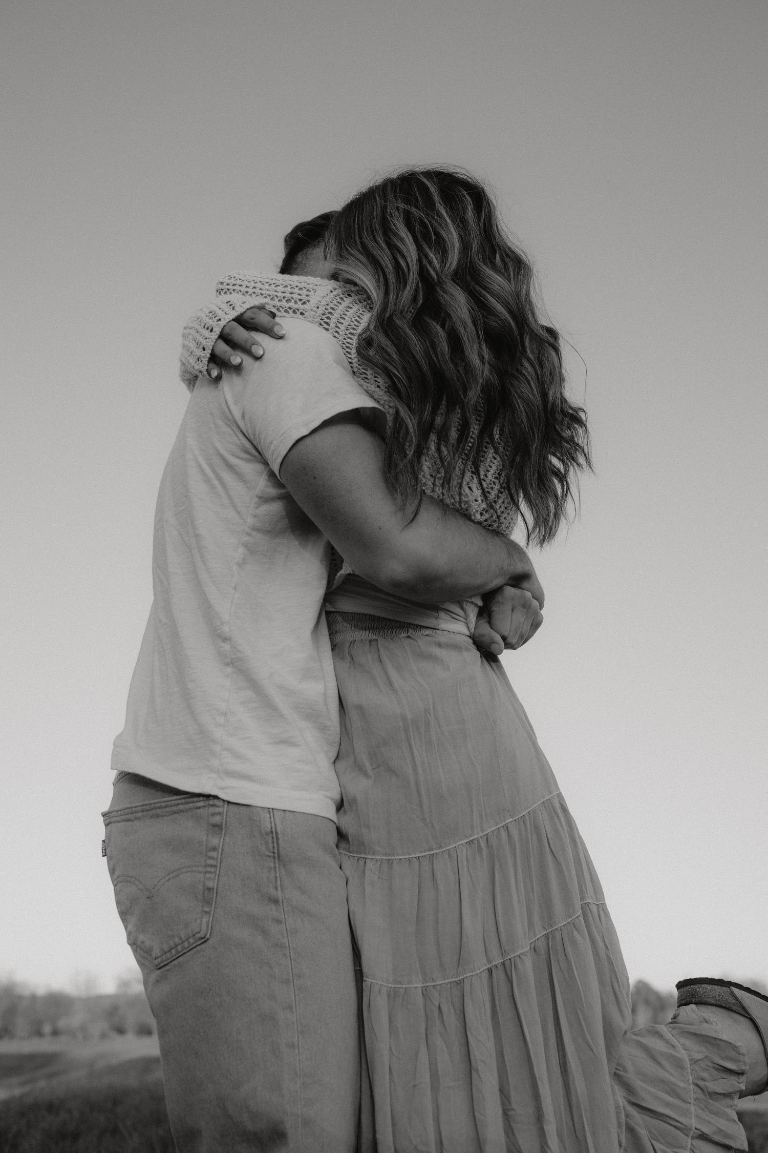 Intimate black and white portrait of couple embracing in casual outdoor setting.