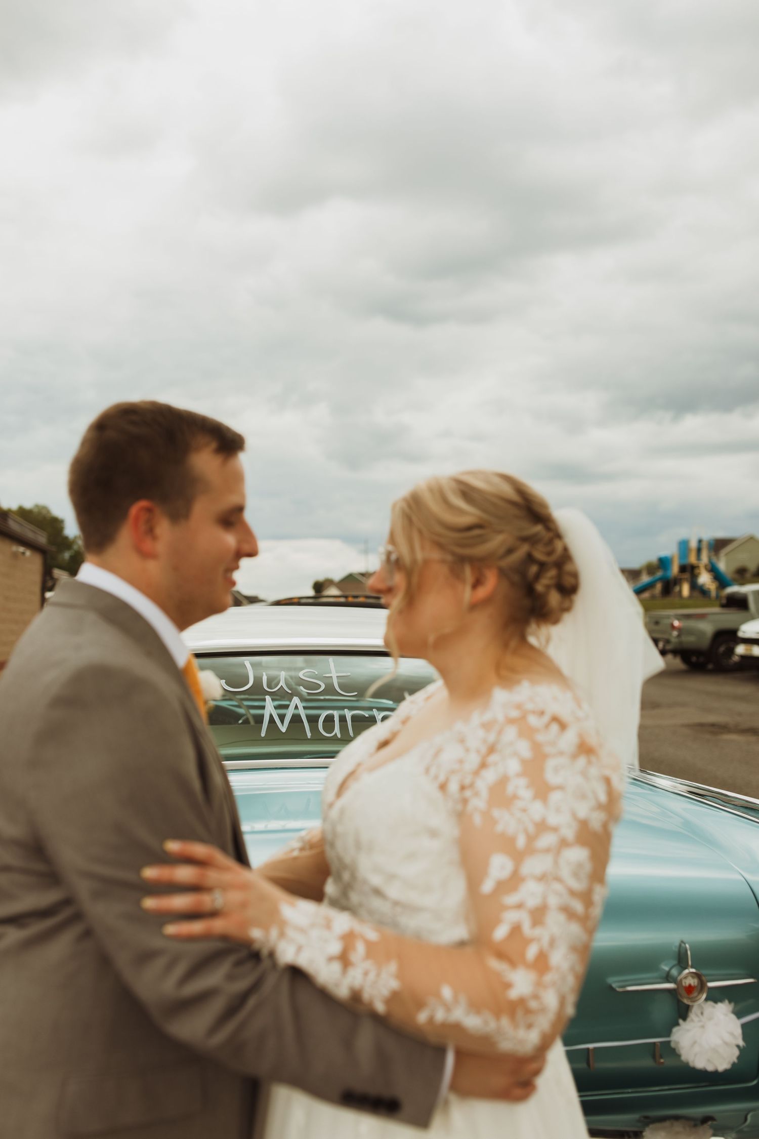A couple shares a romantic moment next to a vintage car decorated with 'Just Married' signage.