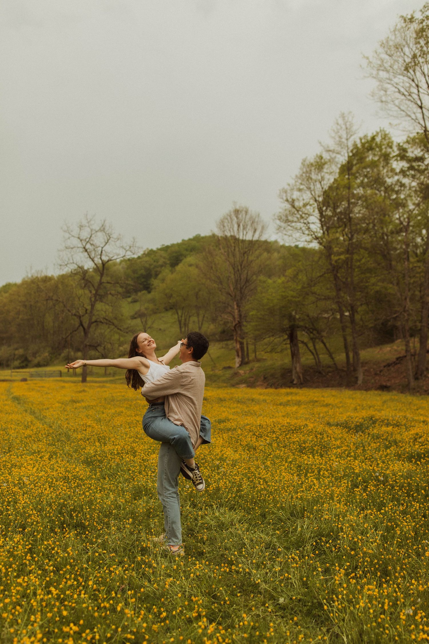 A couple dances playfully in a meadow filled with yellow spring flowers.