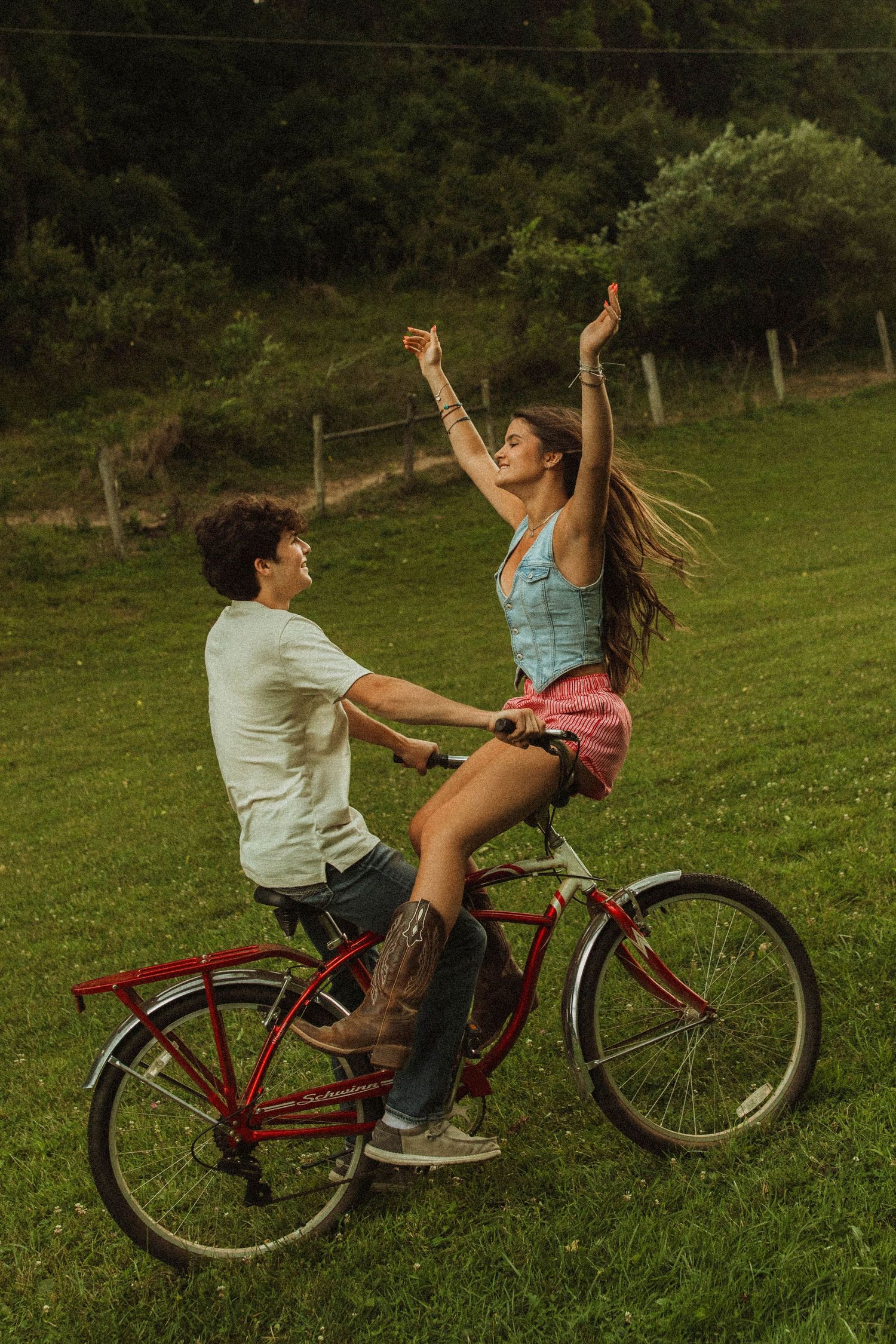 Joyful bicycle ride with arms raised against a green hillside backdrop.