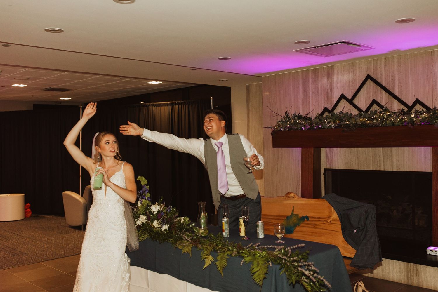 Wedding couple celebrates with raised arms at decorated reception head table.