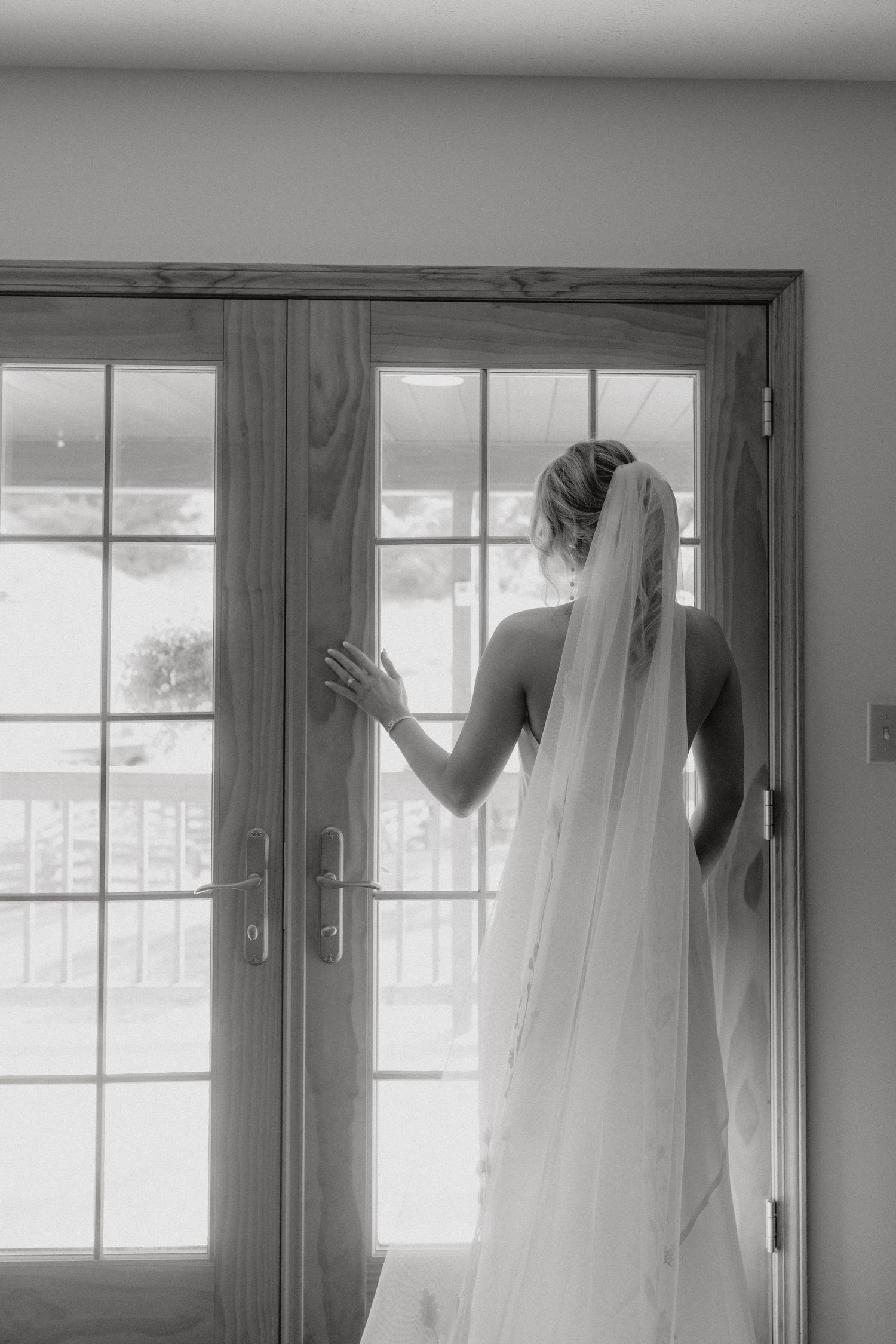 Silhouette of bride in veil looking through French doors in black and white.