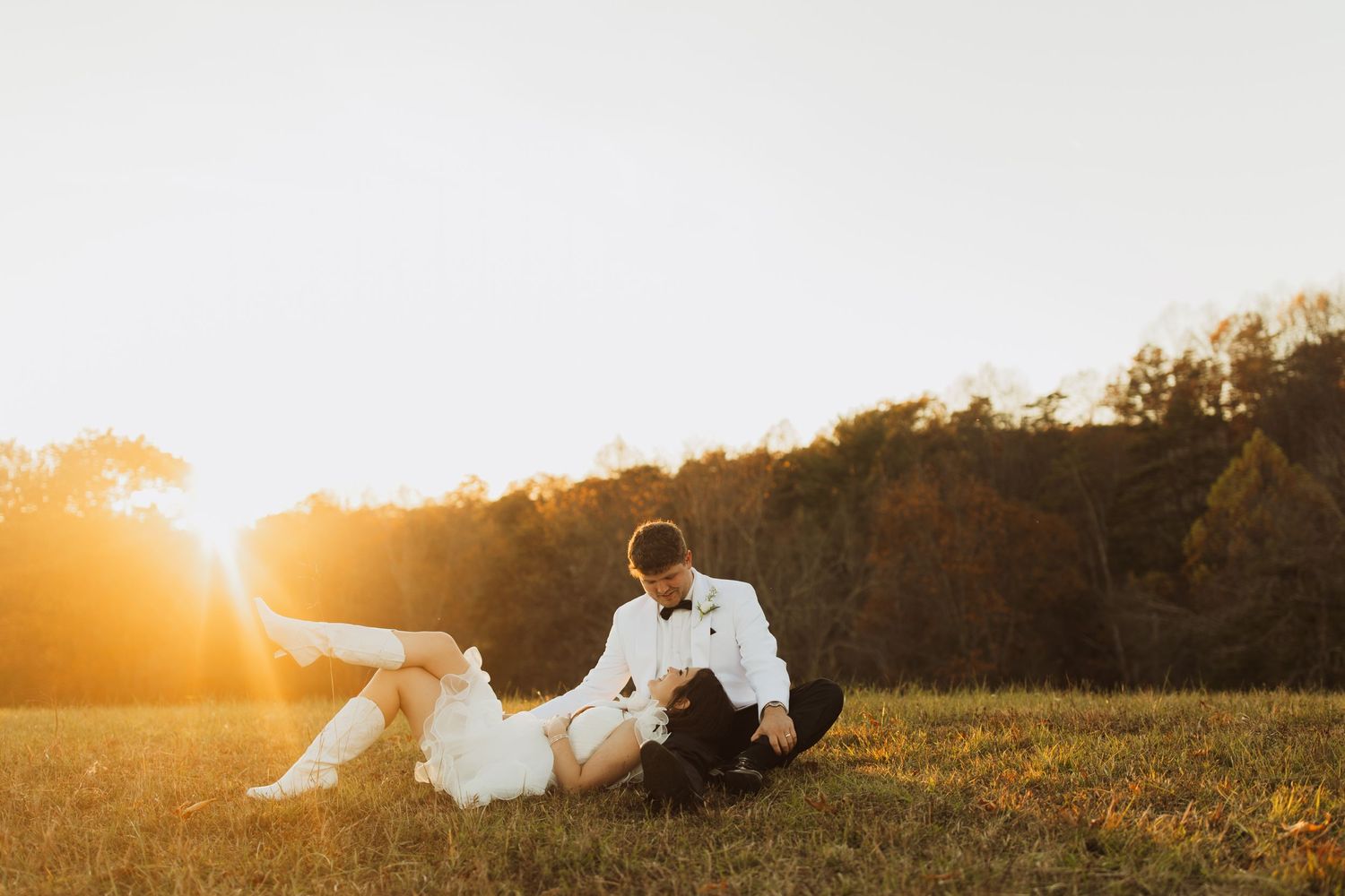 Romantic sunset photo of couple sitting together in golden field during magic hour.