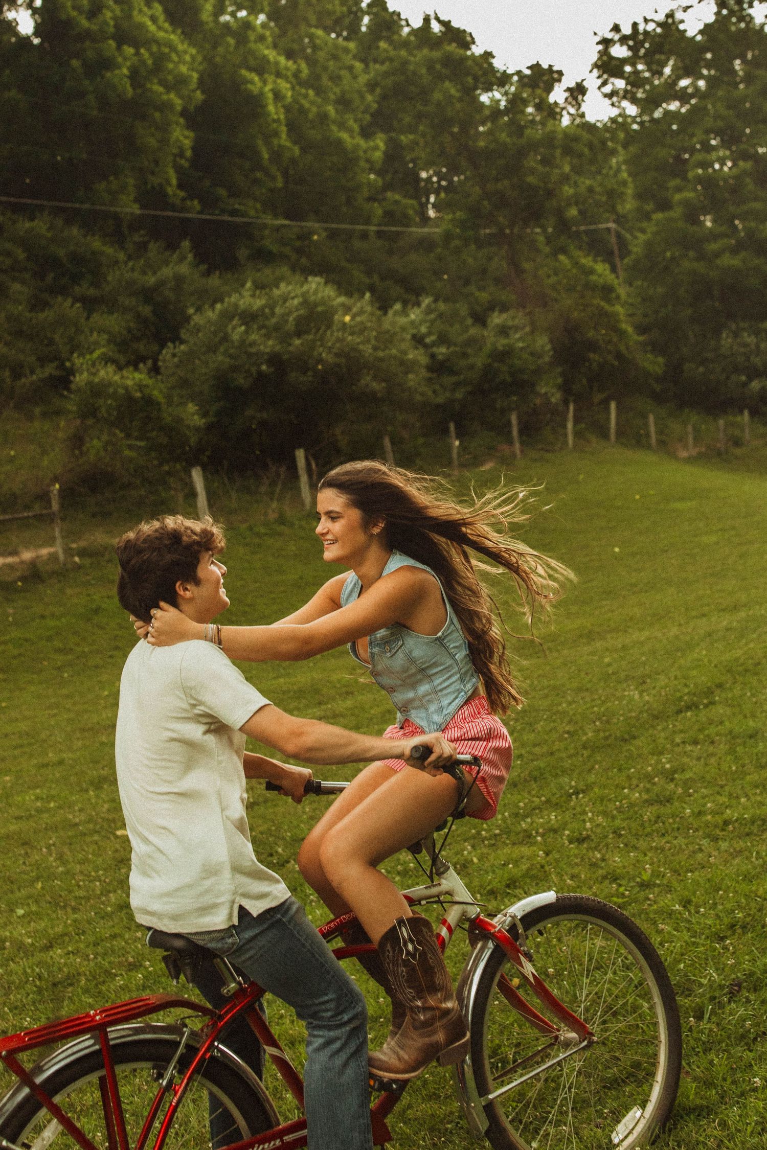 Playful moment shared on a vintage red bicycle in a rural setting.